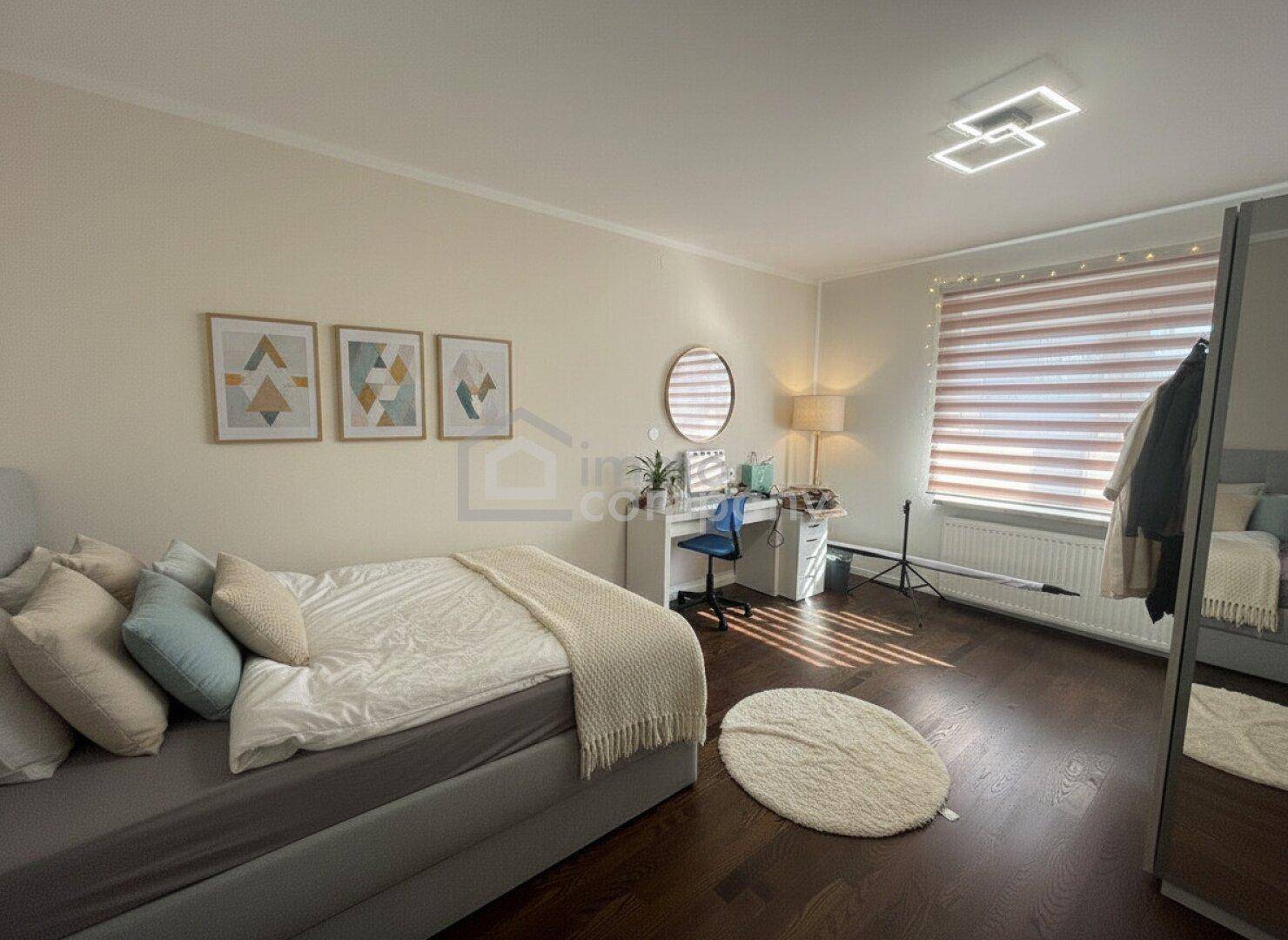 Helles Schlafzimmer mit Schreibtisch, Spiegel und dunklem Holzboden.