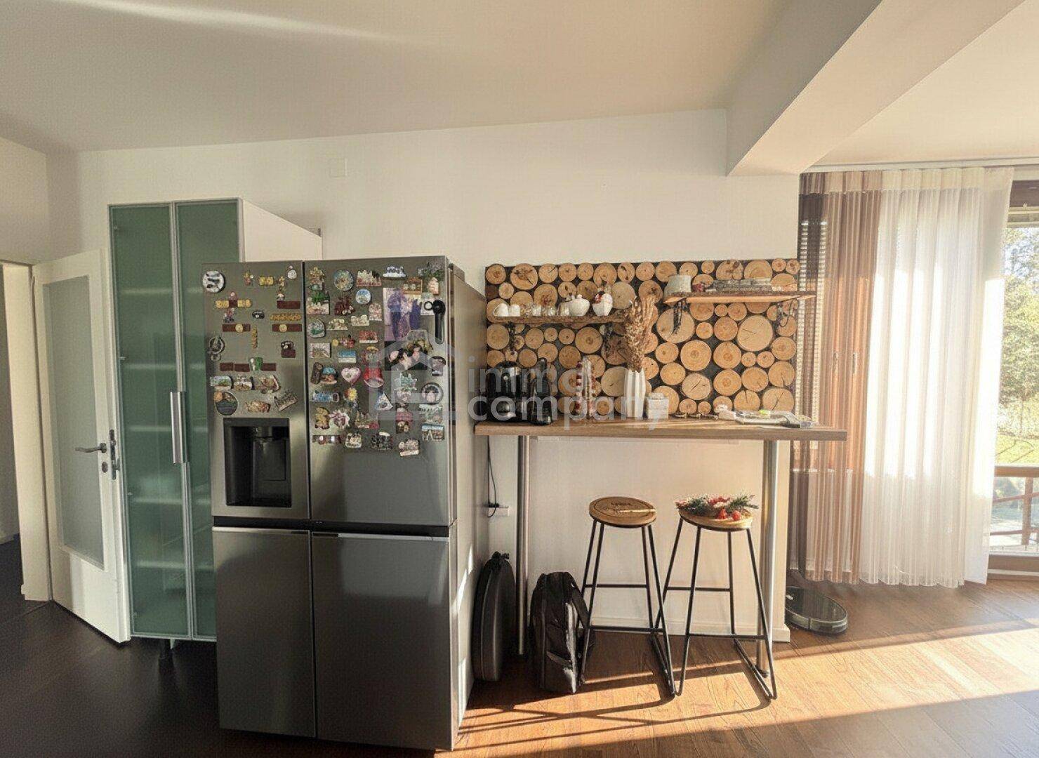 Offener Wohnbereich mit großem Kühlschrank, Frühstücksbar und Zugang zum Balkon.