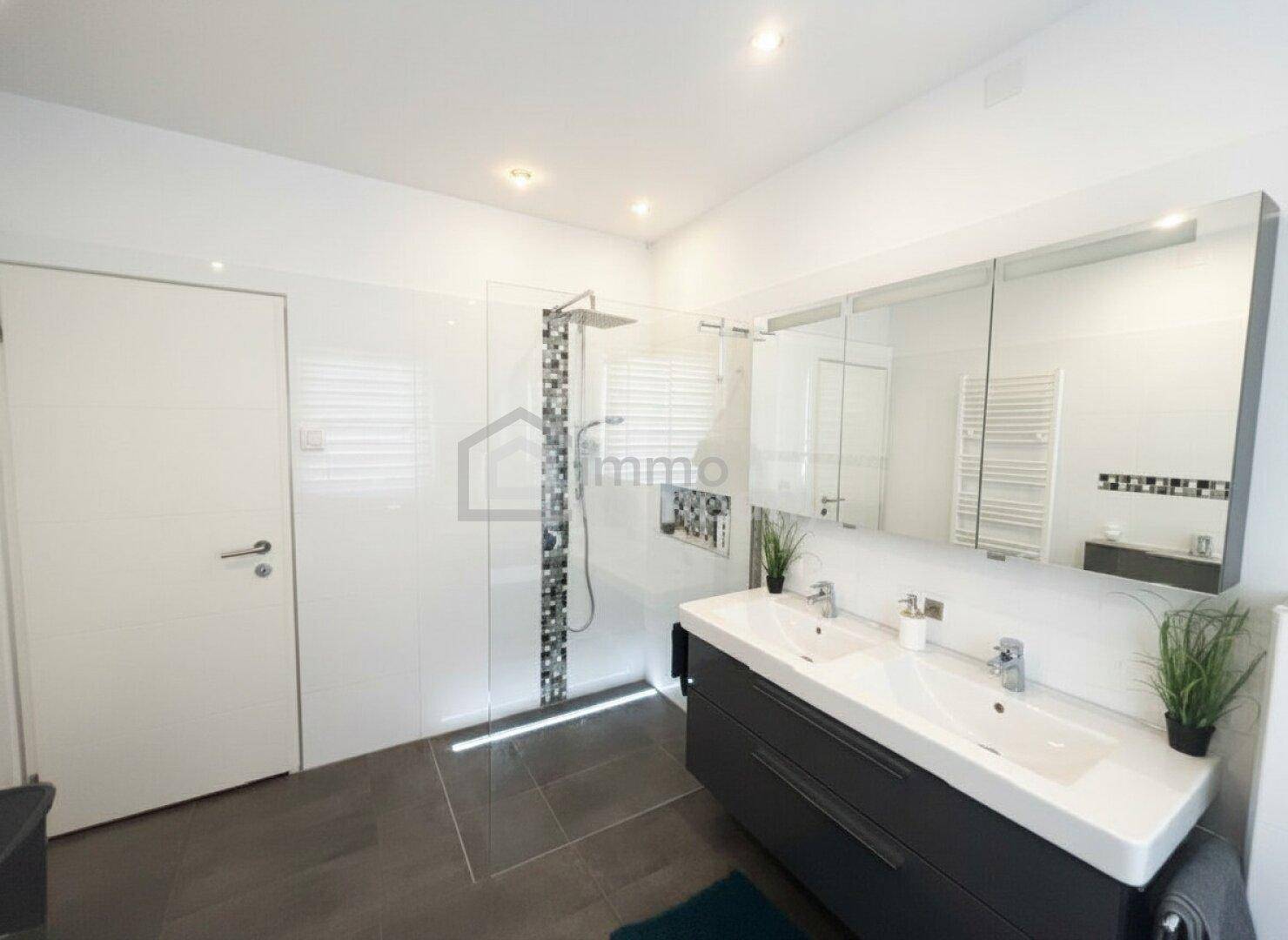 Modernes Badezimmer mit großer begehbarer Dusche, Doppelwaschbecken und weißen Fliesen.