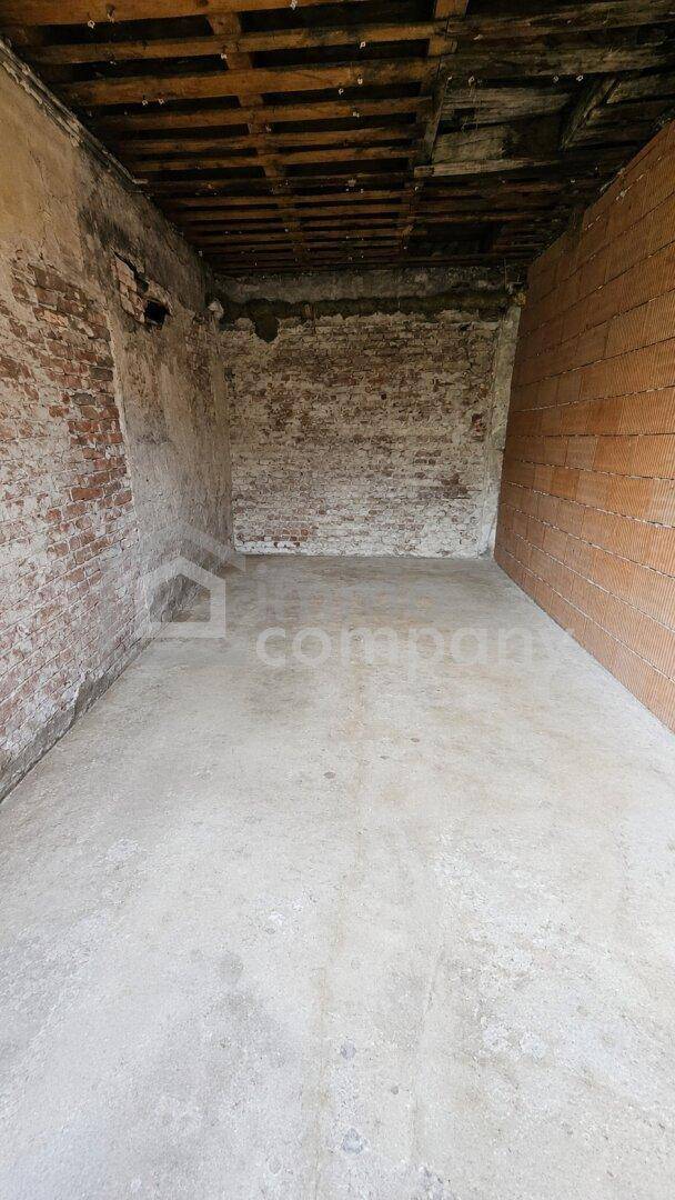 Kellerraum mit Betonboden, freigelegten Ziegelwänden und Holzbalkendecke.
