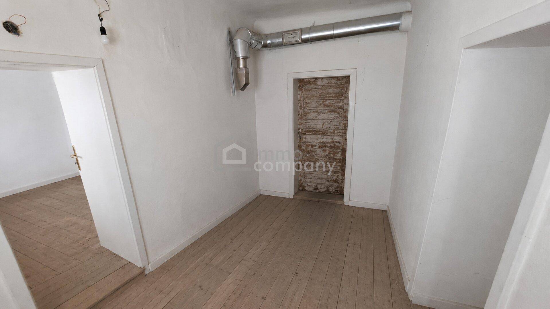 Kleiner Raum mit Holzdielenboden, weiß gestrichenen Wänden und alter Holztür.