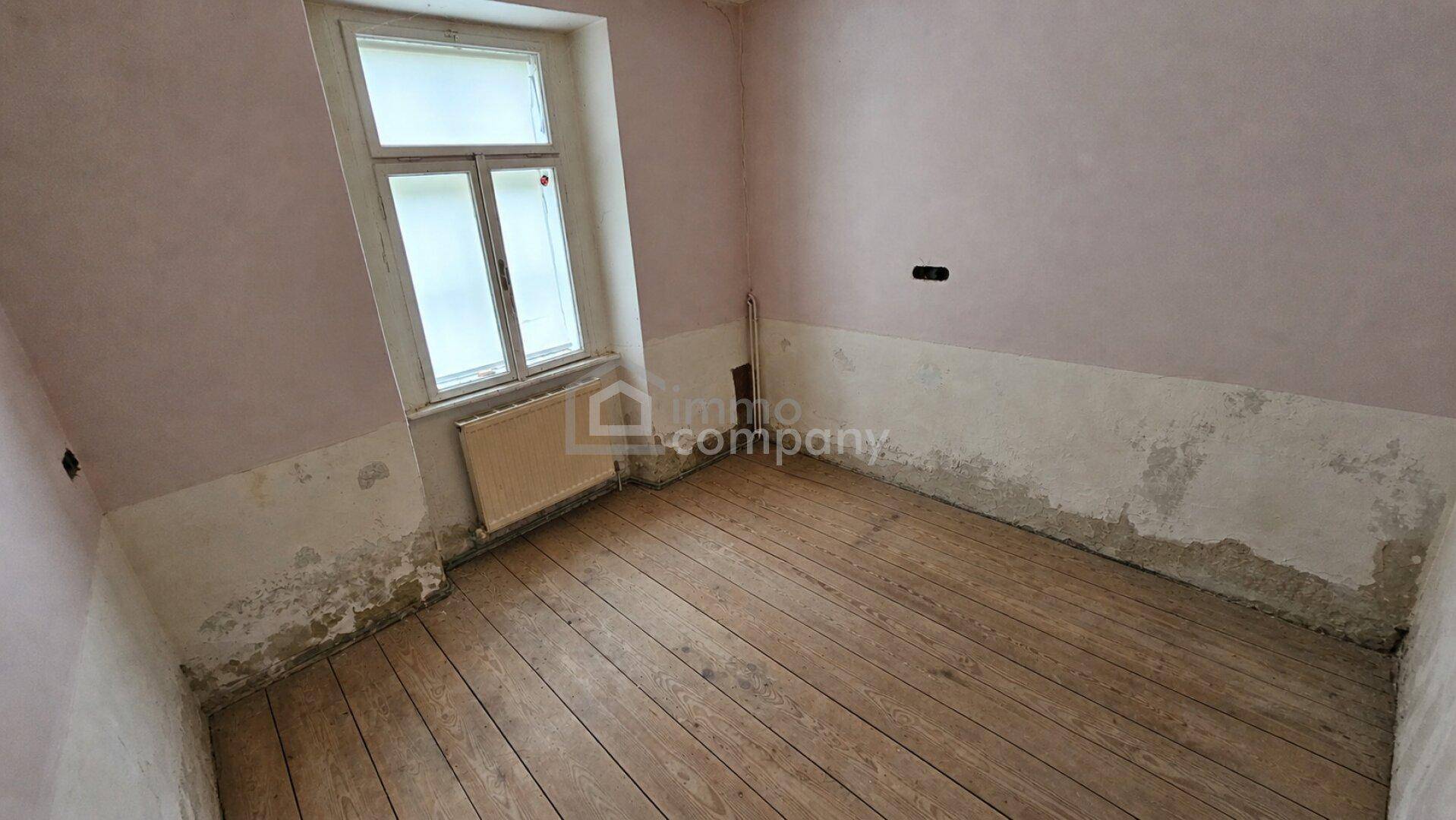 Raum mit Holzdielenboden und teilweise abblätternder Farbe an den Wänden.