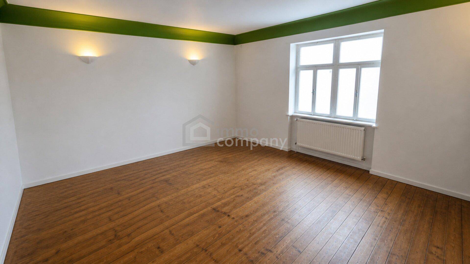 Renovierter Raum mit Holzdielenboden, weißen Wänden und grünem Deckenrand.