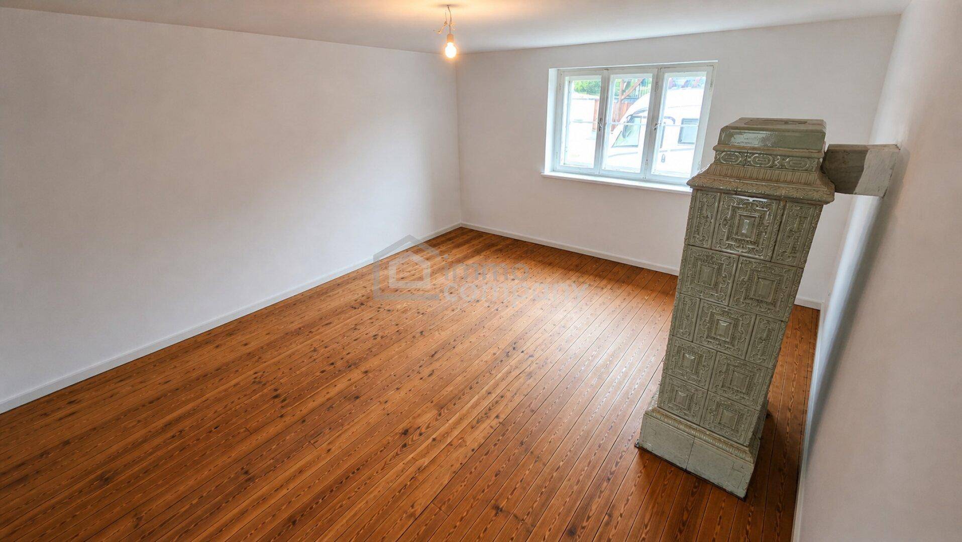 Heller Raum mit Holzdielenboden und einem traditionellen Kachelofen.