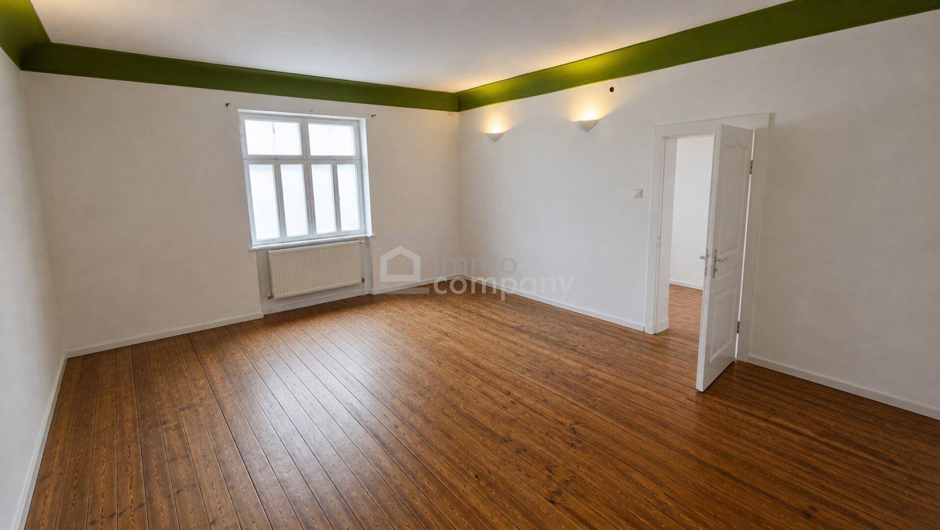Renovierter Raum mit Holzdielenboden, weißen Wänden und grünem Deckenrand.