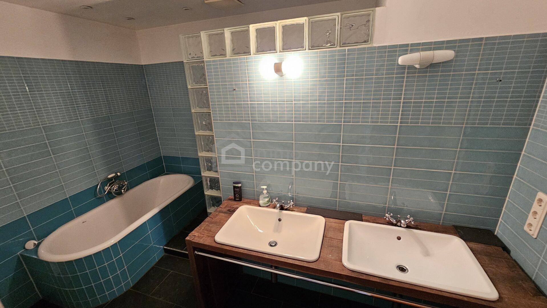 Badezimmer mit blauen Fliesen, Badewanne und Doppelwaschbecken.
