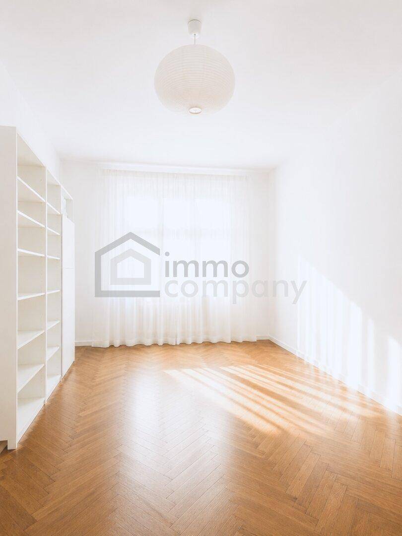 Heller Raum mit Fischgrätparkett, großen Fenstern und weißen Regalen, ideal als Wohn- oder Schlafzimmer.