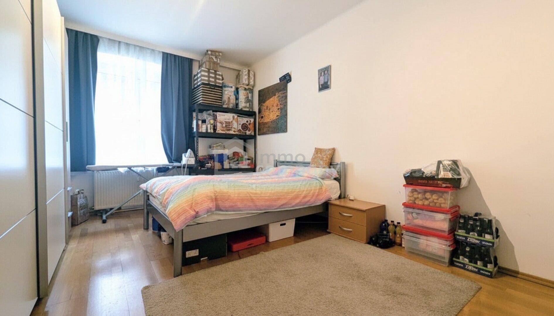 Helles Schlafzimmer mit Holzboden, großem Kleiderschrank und einem Fenster mit blauen Vorhängen.