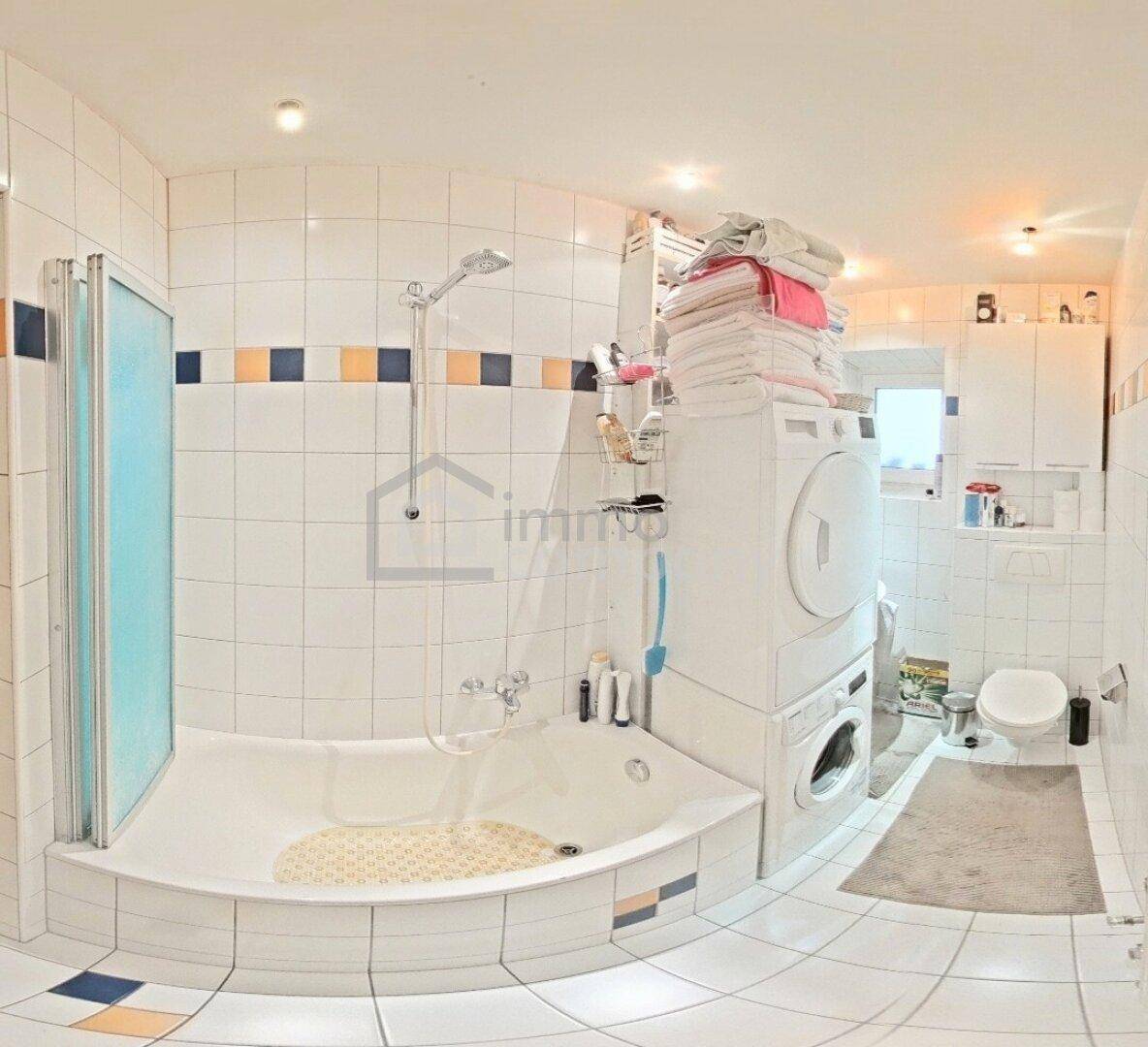 Badezimmer mit Eckbadewanne, Dusche, Toilette und praktischem Waschmaschinen-Trockner-Turm.