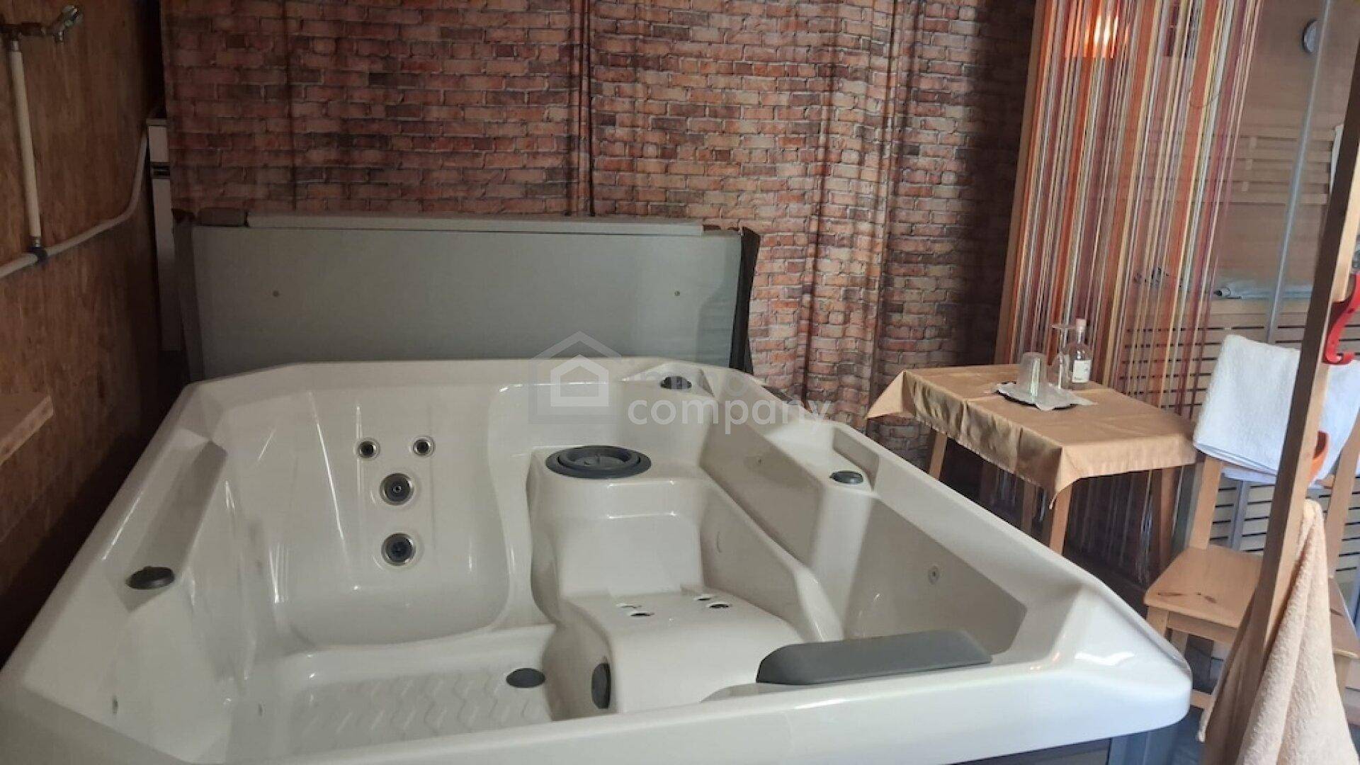 Großer Whirlpool in einem Raum mit Ziegelwand und Beistelltisch für Entspannung.