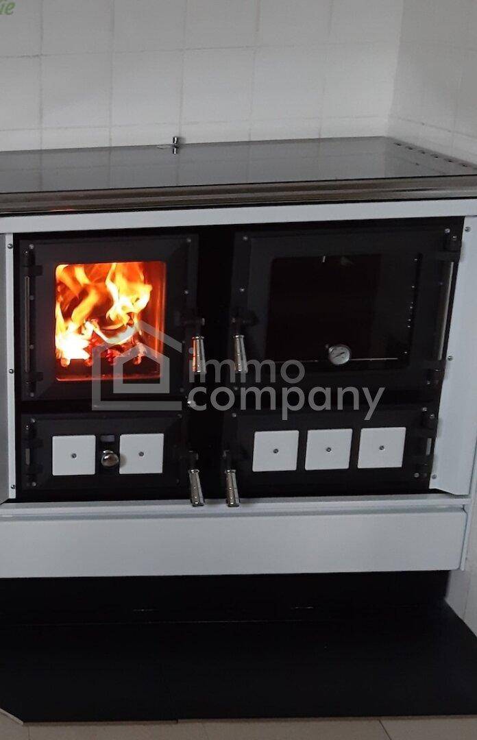 Traditioneller Holzofen mit integriertem Backfach und sichtbarem Feuer in einer Küche.