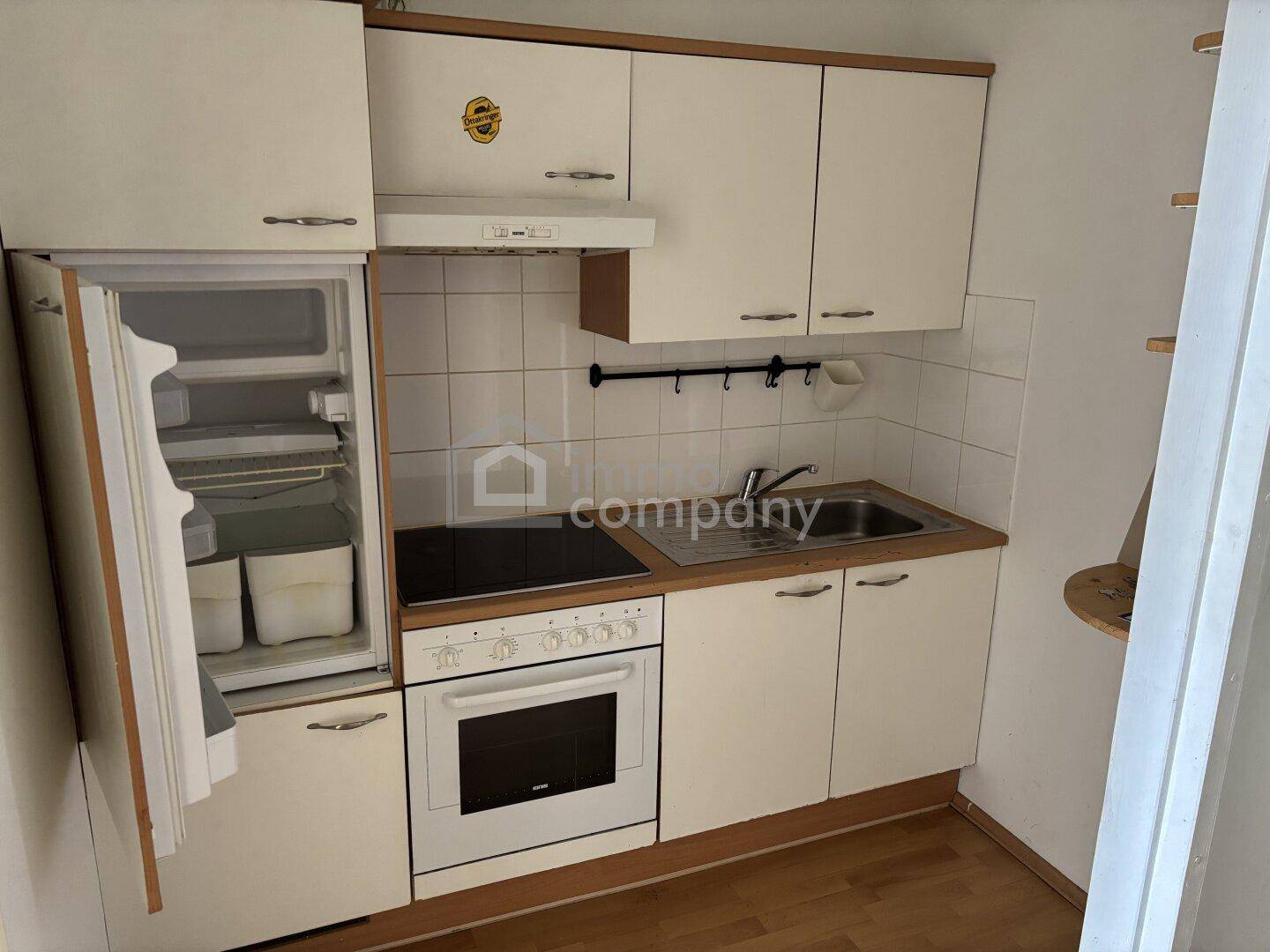 Kleine Küchenzeile mit integriertem Kühlschrank, Kochfeld und Oberschränken.