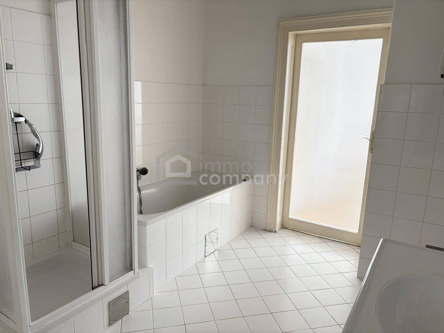 Badezimmer mit Badewanne, separater Duschkabine und weiß gefliesten Wänden und Boden.