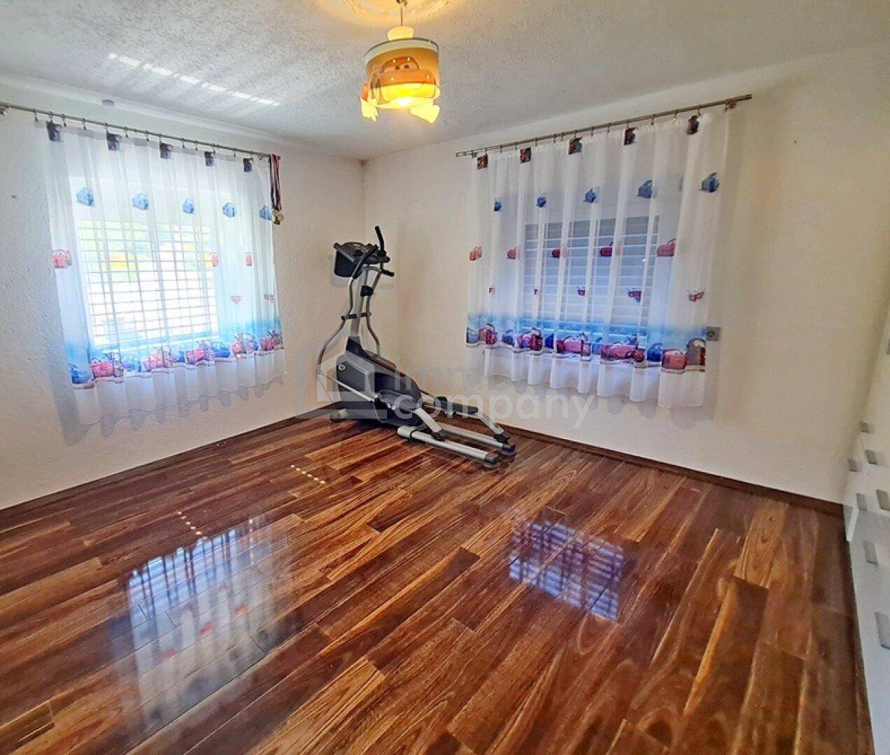 Helles Schlafzimmer mit glänzendem Holzboden und zwei Fenstern.