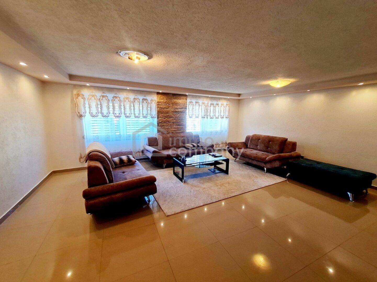 Geräumiges Wohnzimmer mit Fliesenboden, bequemen Sofas und dekorativer Wandverkleidung.