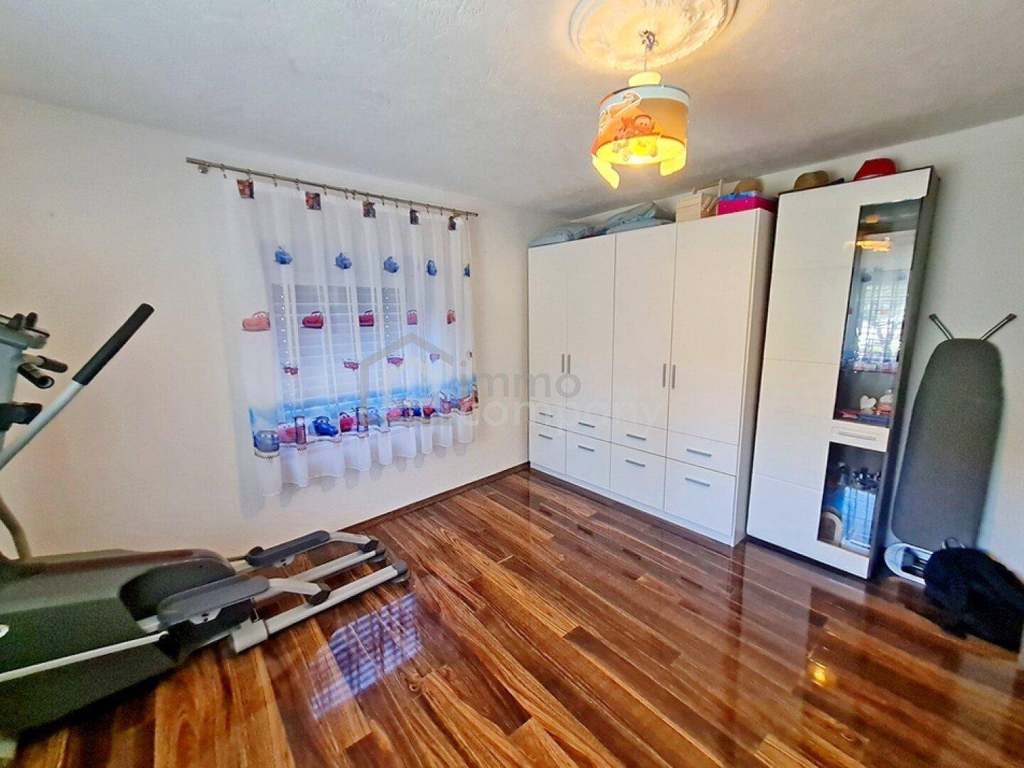 Schlafzimmer mit Holzboden, weißen Schränken und einem Fitnessgerät.