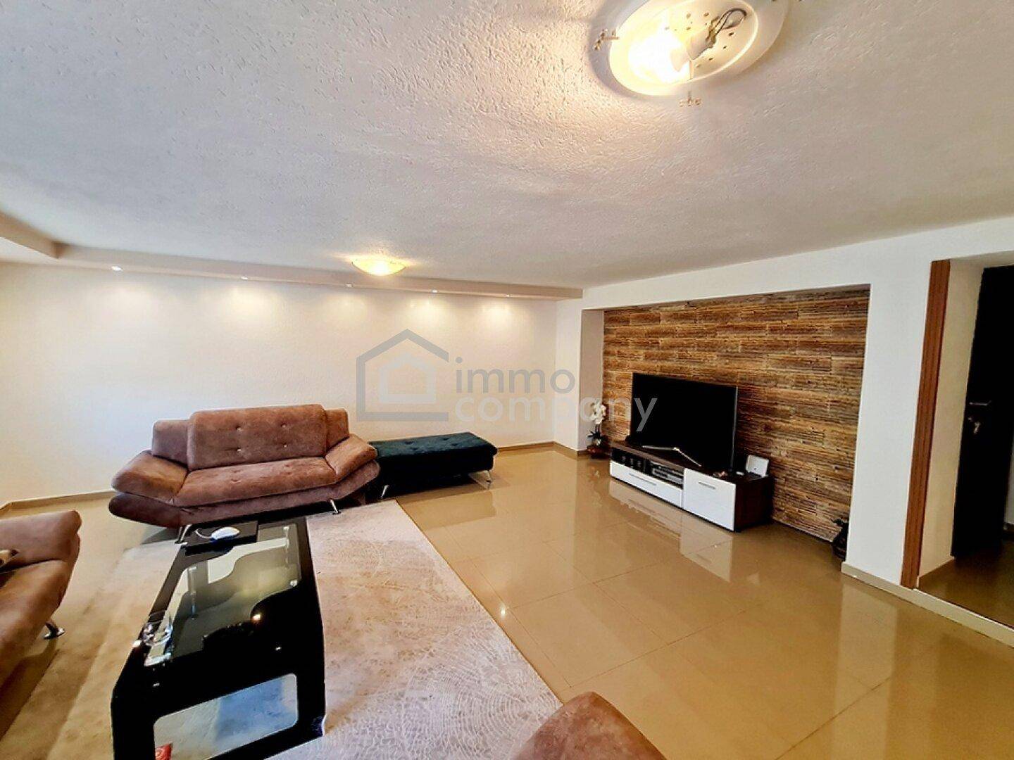 Wohnzimmer mit Fliesenboden, Fernseher und einer Wand mit Holzverkleidung.