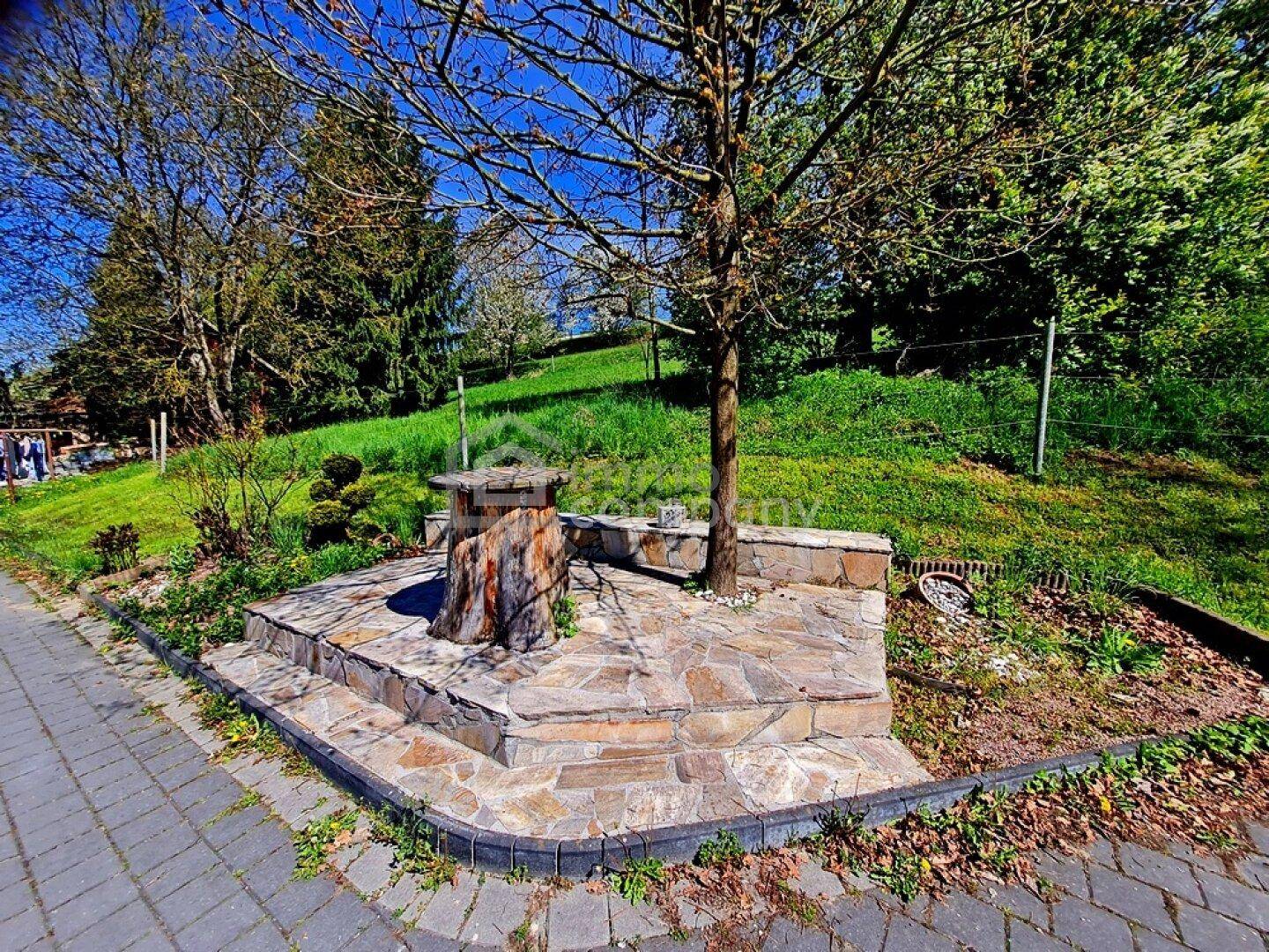 Steingepflasterter Sitzbereich im Garten mit Baum und grüner Umgebung.
