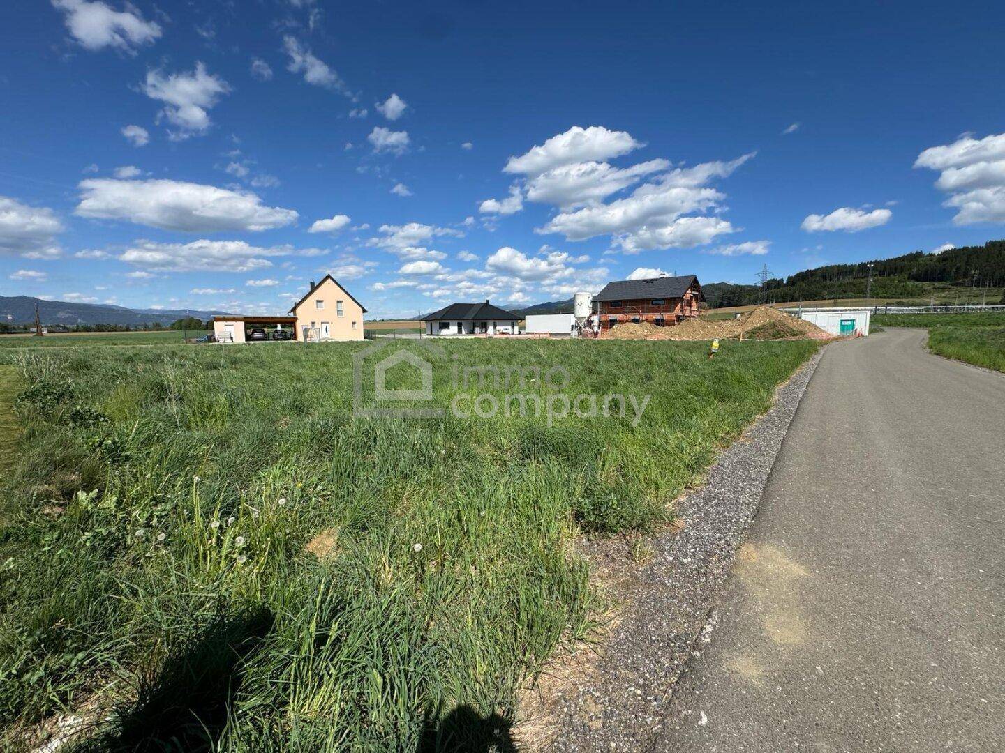 Großes grünes Grundstück mit Blick auf umliegende Häuser und die Berglandschaft unter strahlendem Himmel.