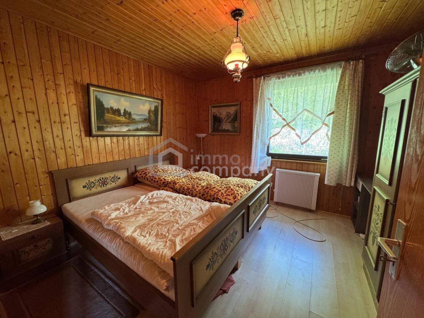 Schlafzimmer mit gemütlicher Holzvertäfelung, Doppelbett und Fenster mit Blick ins Grüne.