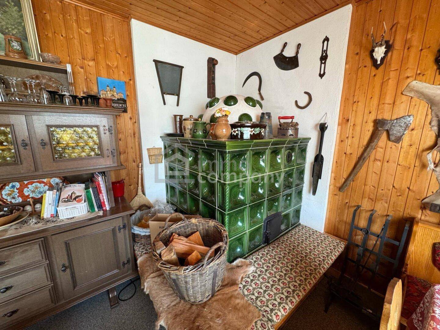 Traditioneller grüner Kachelofen in einer Ecke des Wohnbereichs, umgeben von rustikalen Dekorationen.