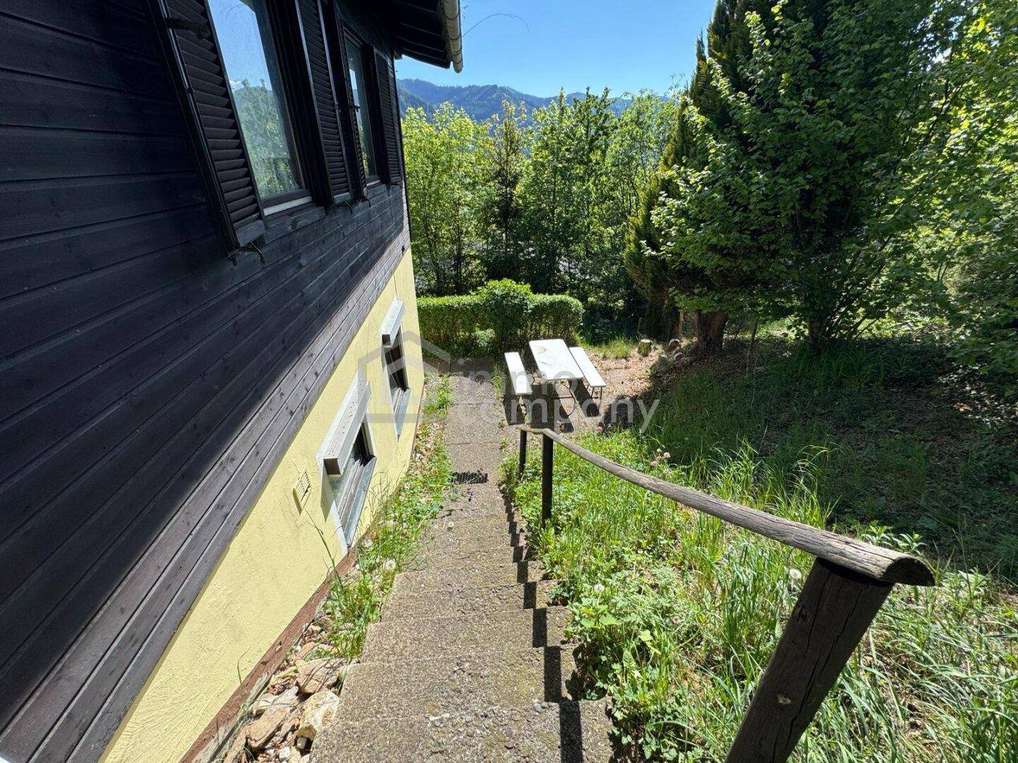 Betontreppe führt entlang des Hauses hinunter zu einem Picknickbereich im Grünen.