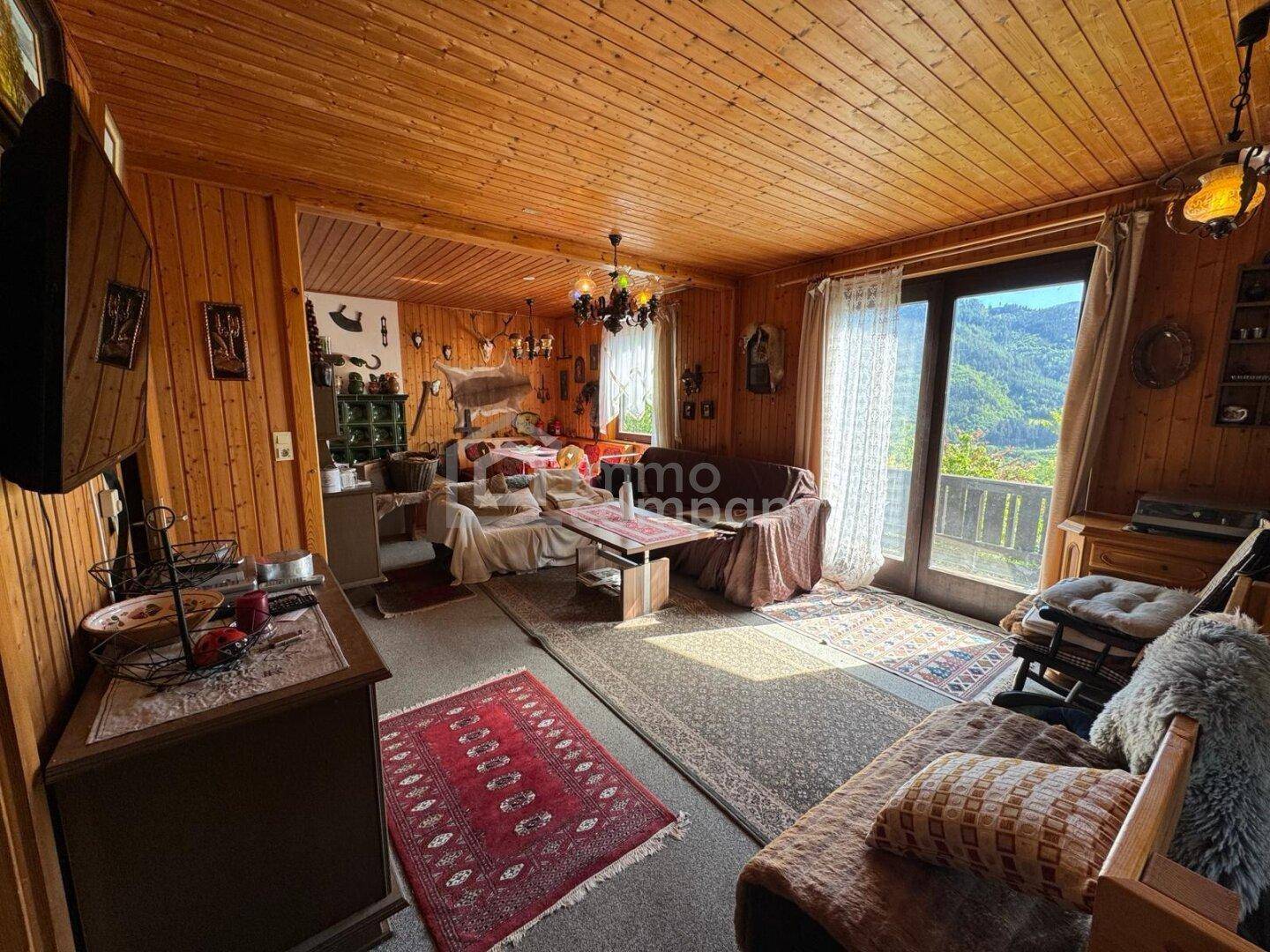 Rustikales Wohnzimmer mit Holzvertäfelung, traditionellen Möbeln und Zugang zu einem Balkon mit Bergblick.
