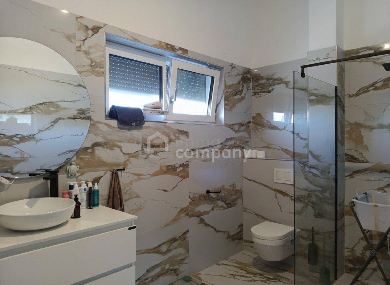 Modernes Badezimmer mit eleganten Marmorfliesen, bodengleicher Dusche und wandhängendem WC.