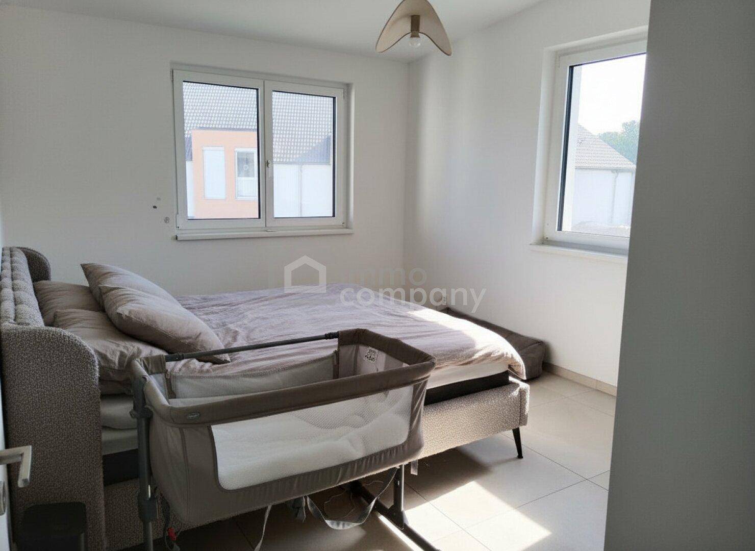 Gemütliches Schlafzimmer mit Doppelbett, Babybett und zwei Fenstern für viel Helligkeit.