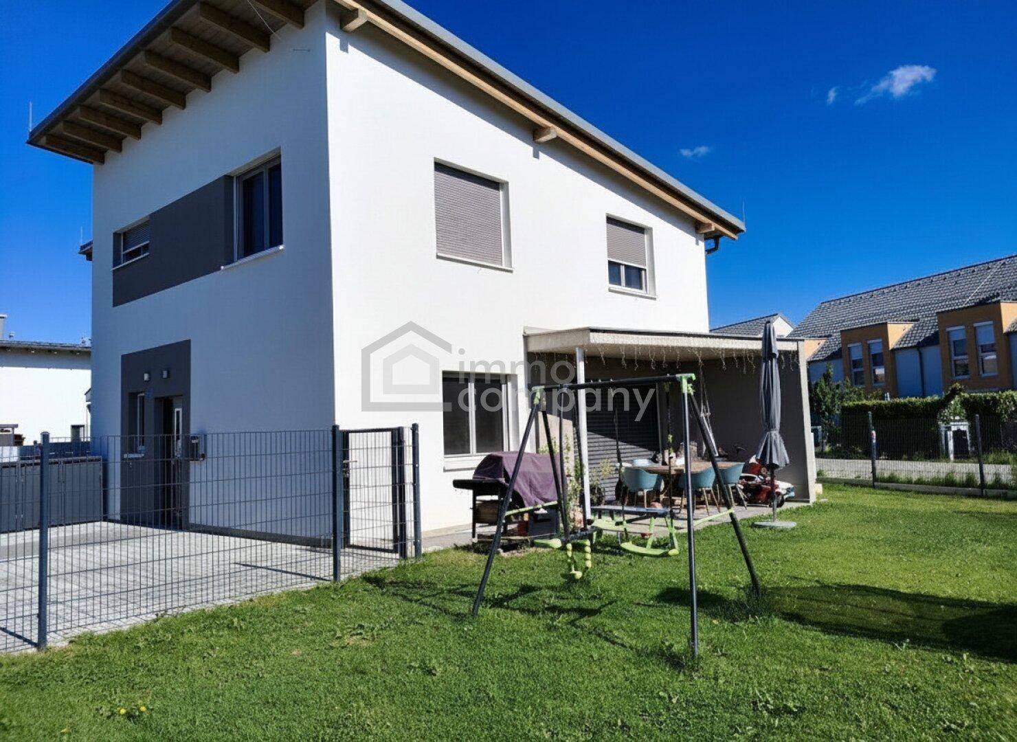 Rückseite des Hauses mit überdachter Terrasse, Rasenfläche und Kinderschaukel im Garten.