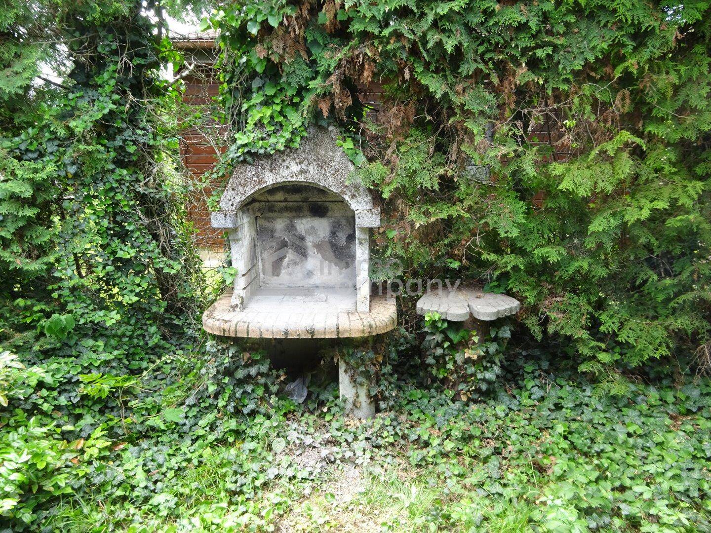 Rustikale Grillstelle aus Stein, umgeben von dichtem Efeu und Bäumen, ideal für Gartenpartys.