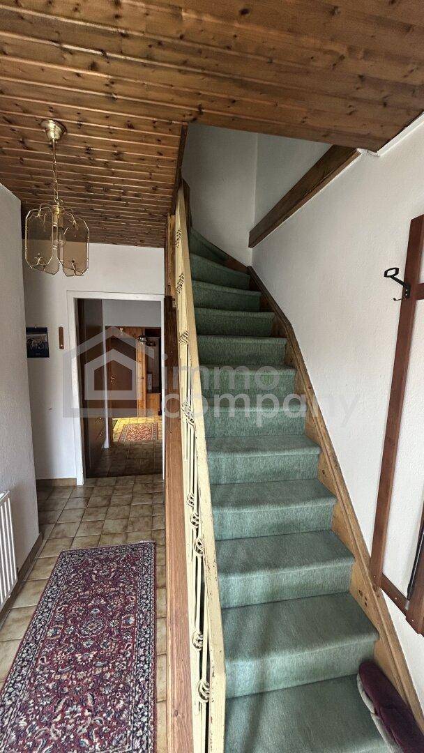 Flur mit Holzdecke und einer Treppe, die mit grünem Teppich ausgelegt ist, dazu ein traditioneller Teppich.