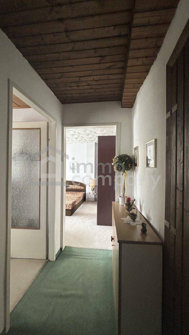 Flur mit grünem Teppichläufer und einer Holzkonsole, der zu einem Schlafzimmer führt.