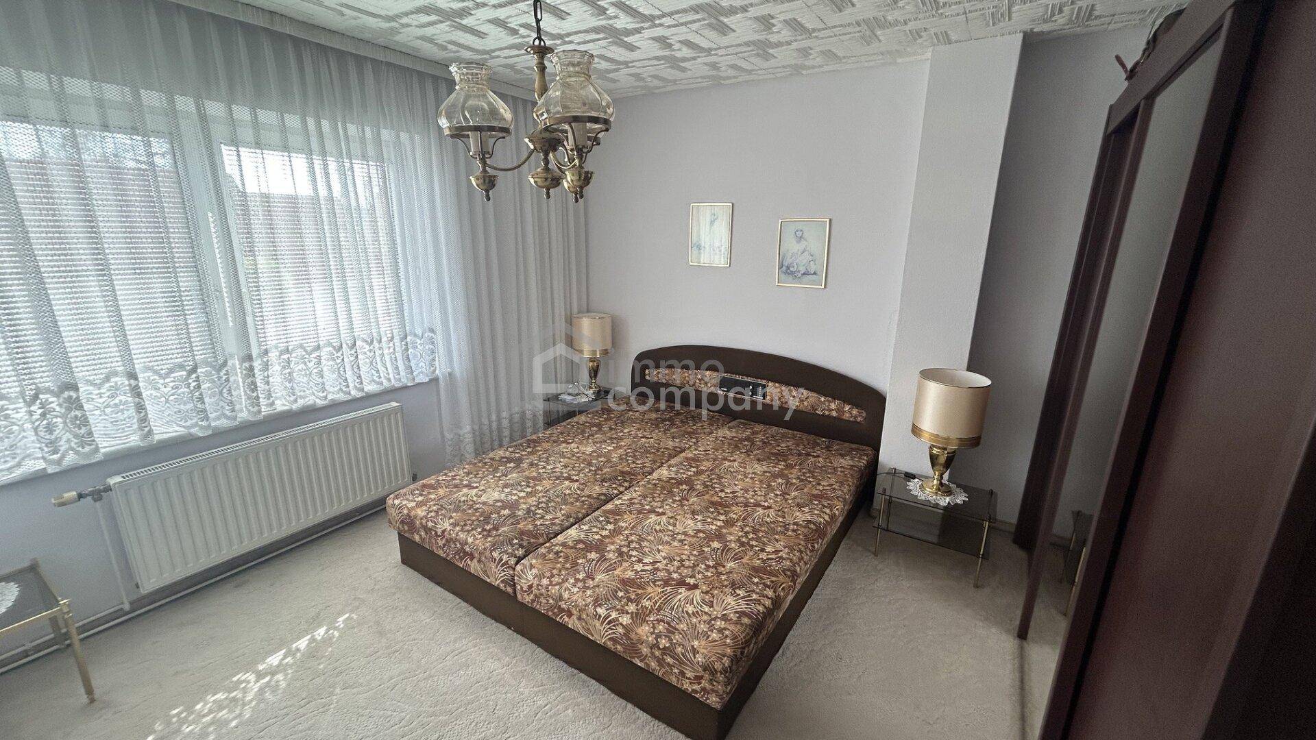 Schlafzimmer mit Doppelbett, Nachttischen und Kleiderschrank, hell durch großes Fenster.