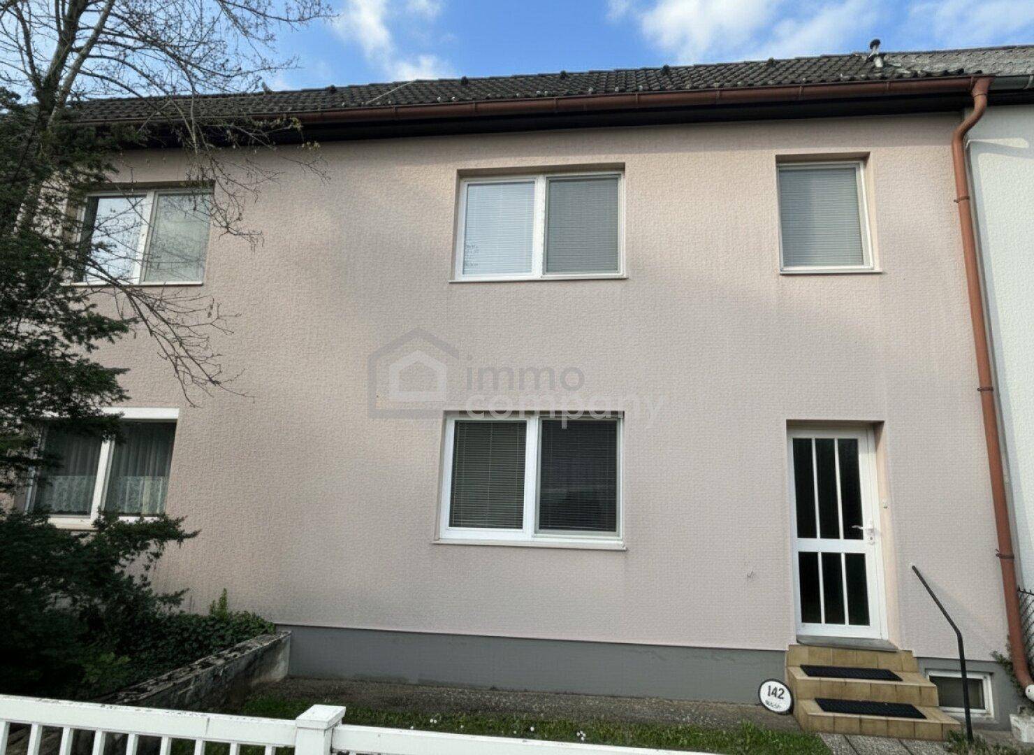 Rückseite eines Hauses mit mehreren Fenstern und einem Eingang, die Fassade ist hell verputzt.