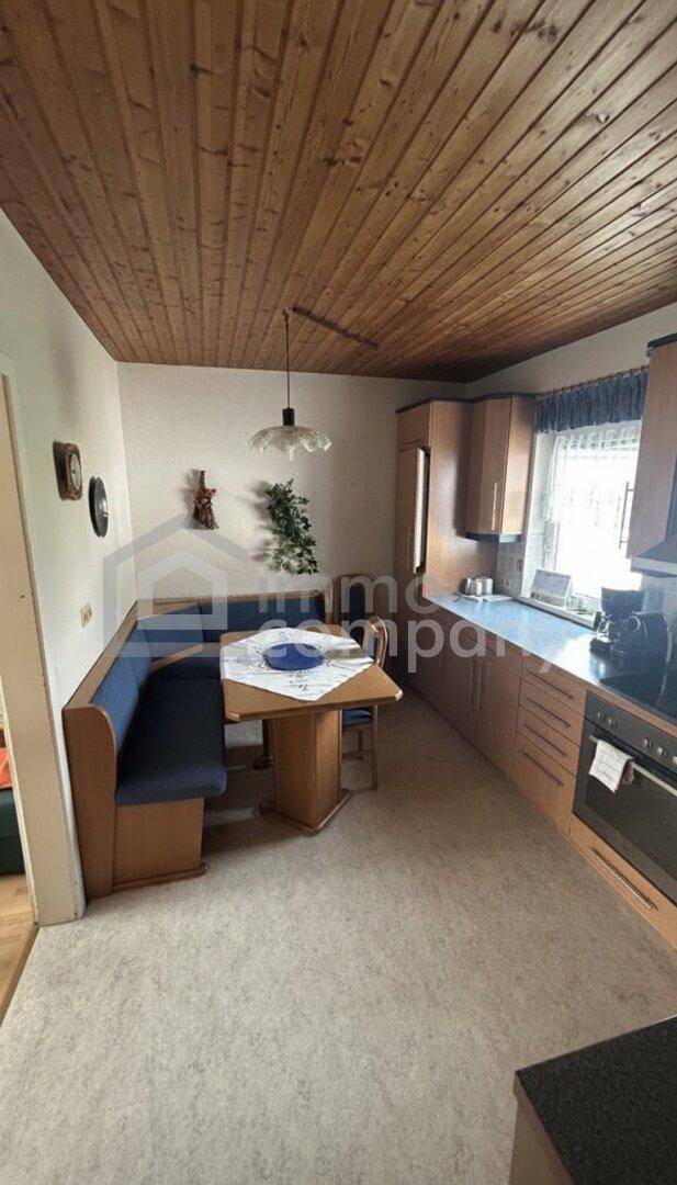 Gemütliche Küche mit integrierter Essecke, Holztisch und blauer Sitzbank unter einer Holzdecke.