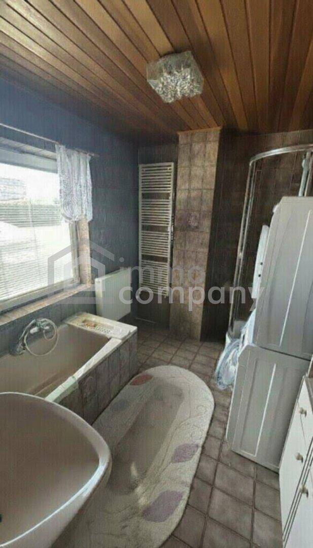 Badezimmer mit Badewanne, Waschbecken und beheiztem Handtuchhalter, gefliest und mit Holzdecke.