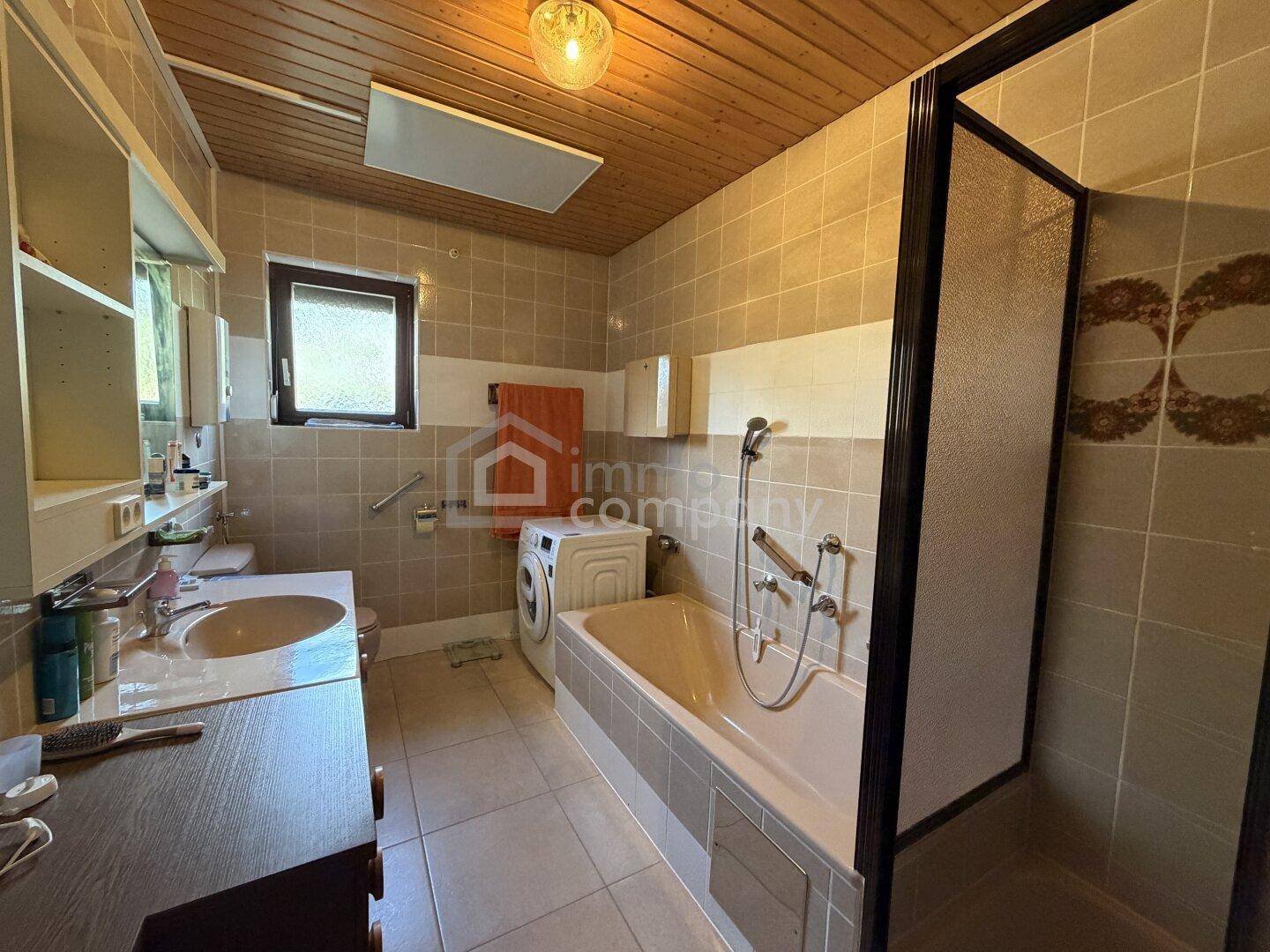 Badezimmer mit Badewanne, Dusche, Waschbecken und Holzdecke in traditionellem Stil der 80er Jahre.