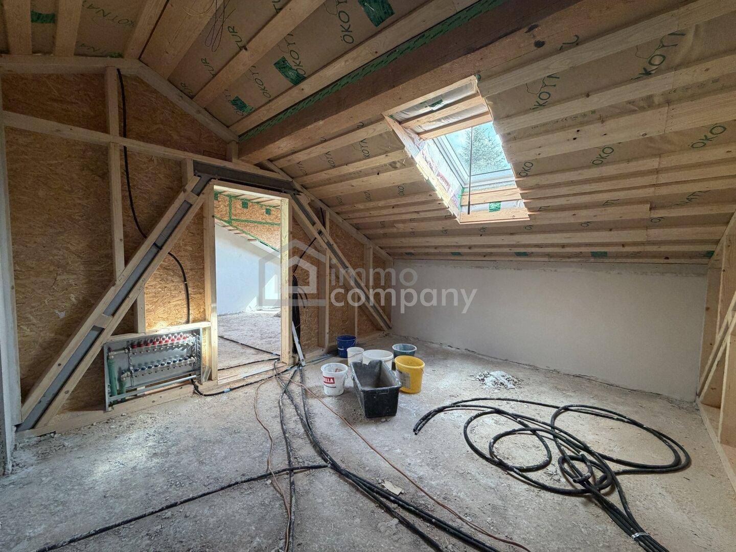 Dachgeschoss im Rohbau mit sichtbaren Holzbalken und Dachfenster für zukünftigen Ausbau.