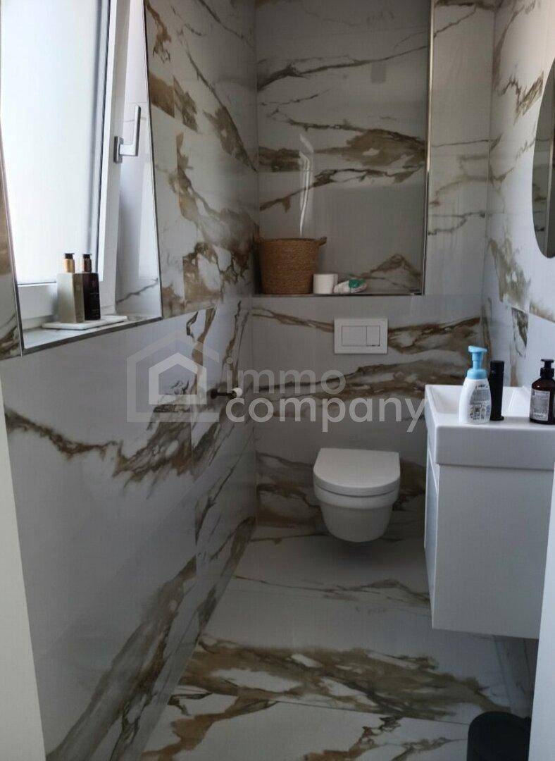 Kleines Badezimmer mit eleganten Marmorfliesen, wandhängendem WC und modernem Waschbecken.