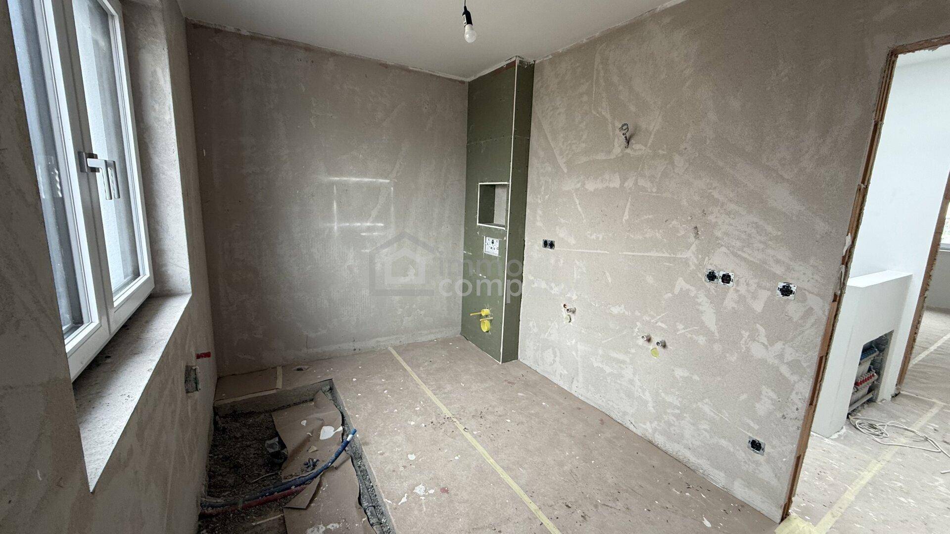Unfertiges Badezimmer mit Fenster und vorbereiteten Anschlüssen für die Installation.