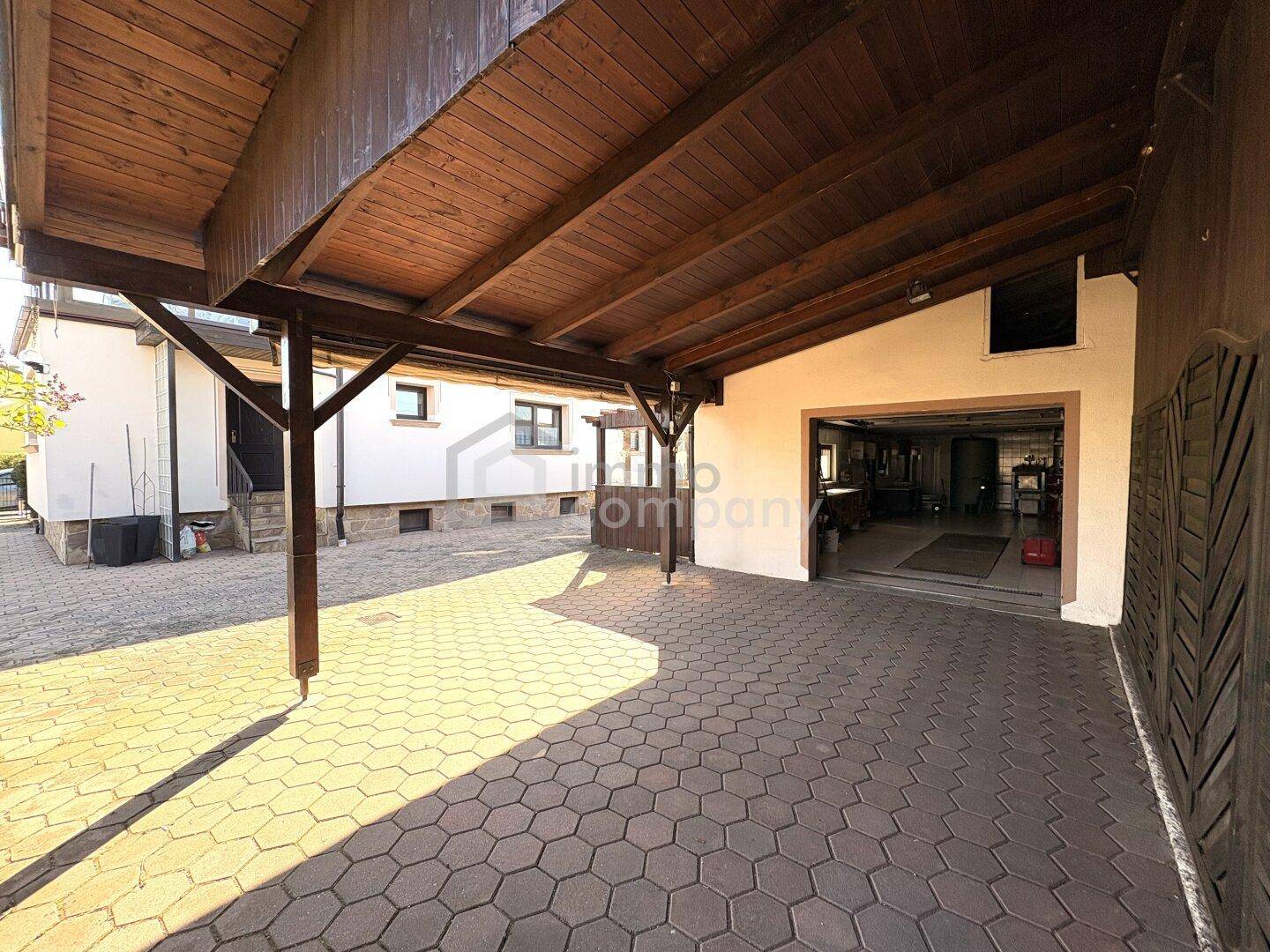 Überdachter Carport-Bereich mit gepflasterter Einfahrt und Zugang zur Garage des Hauses.