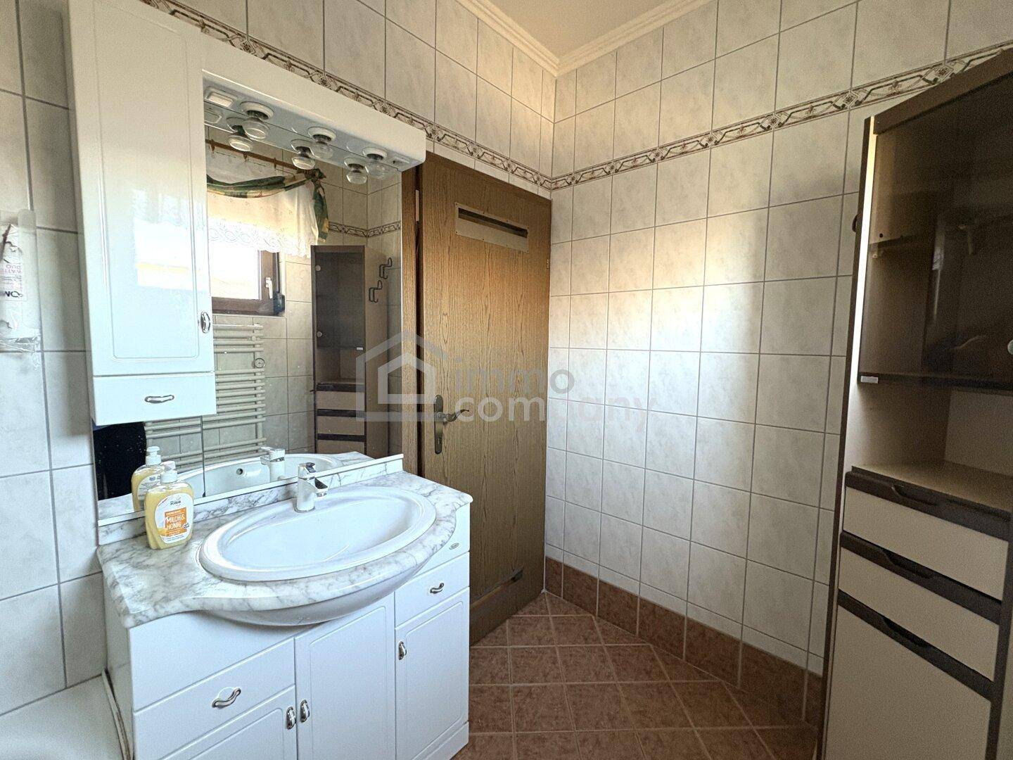 Badezimmer mit Waschbecken, Spiegelschrank und hellen Fliesen, die eine freundliche Atmosphäre schaffen.