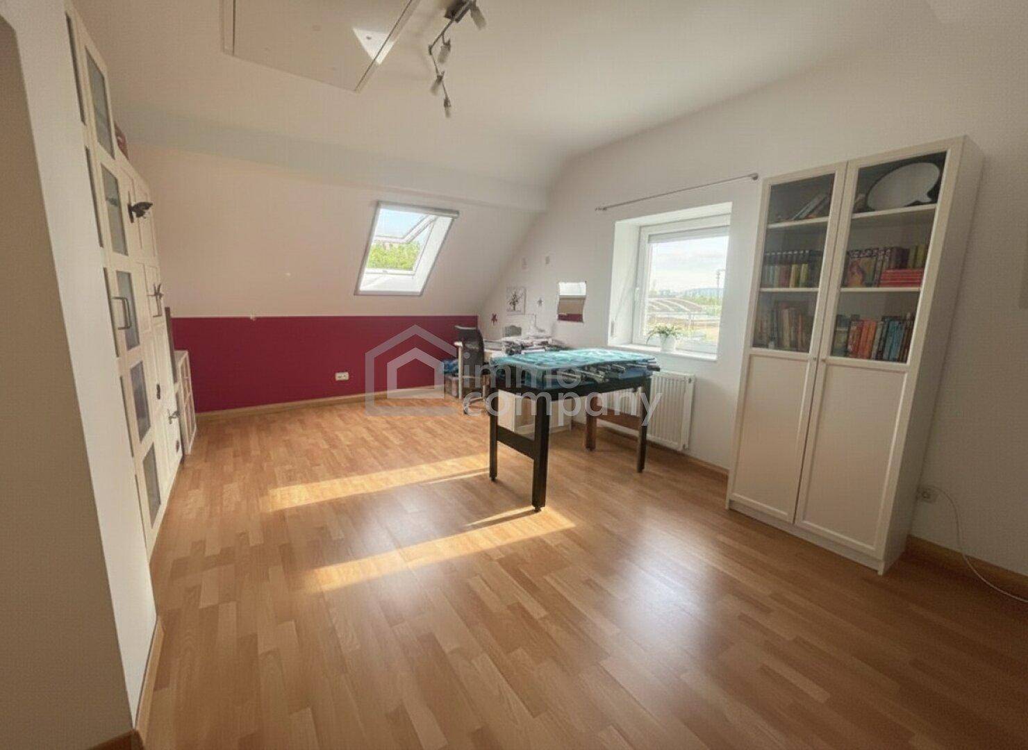 Geräumiges Büro mit Holzboden, Schreibtisch, Bücherregalen und Dachfenster, ideal zum Arbeiten.