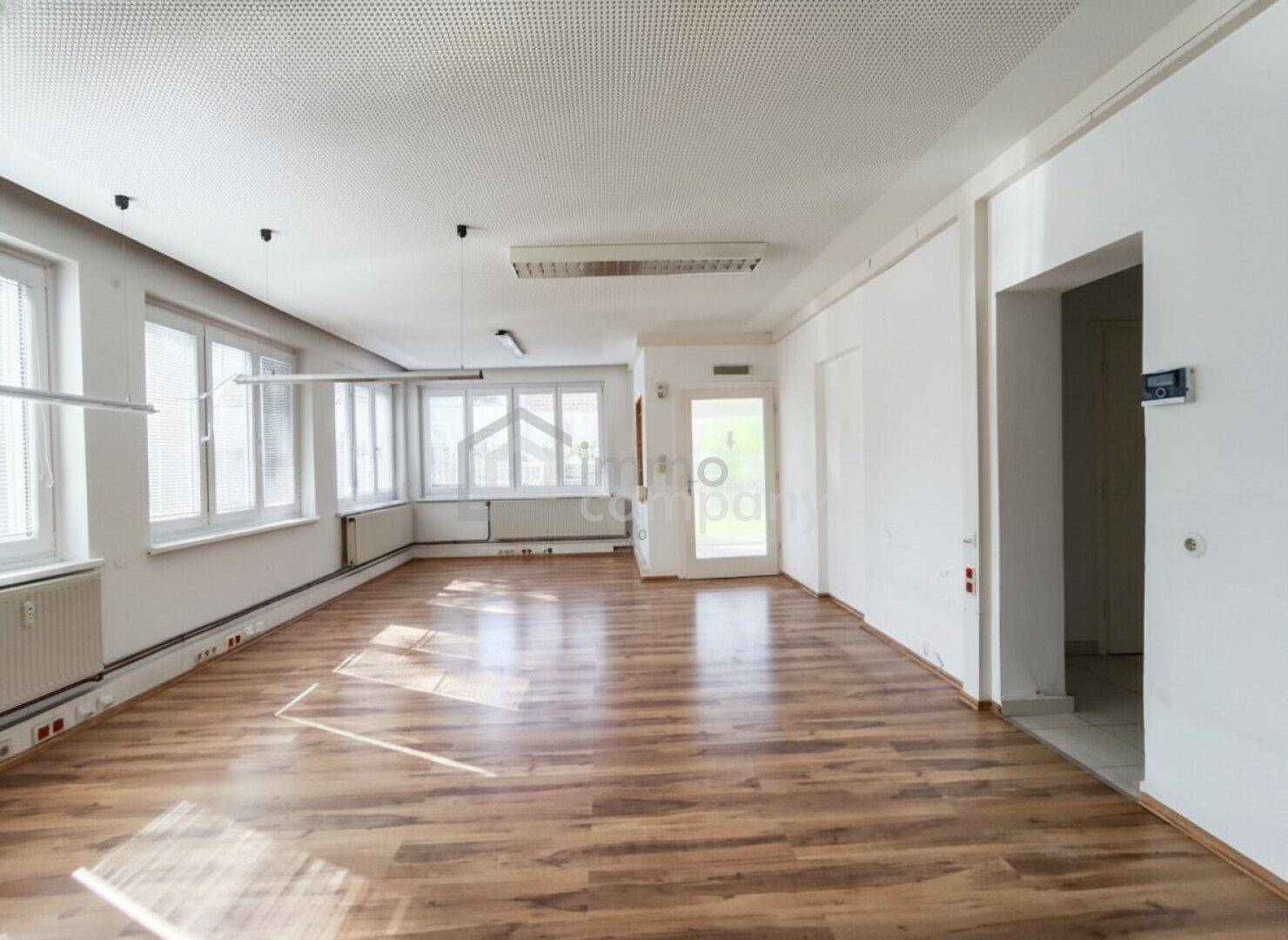 Geräumiger, heller Raum mit Laminatboden und vielen Fenstern, geeignet für Bürozwecke.