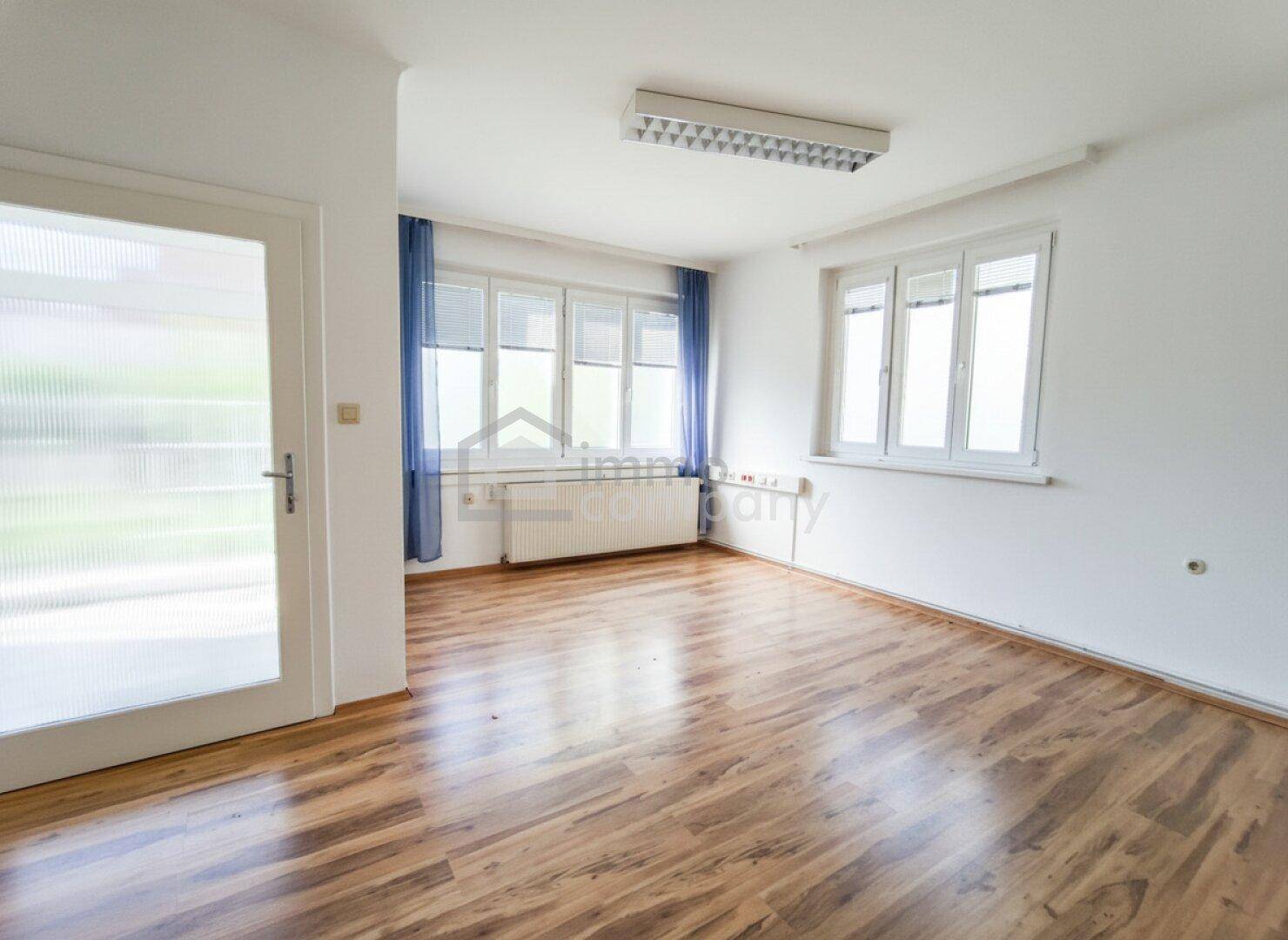 Heller Raum mit Laminatboden und großen Fenstern, ideal als Büro oder vielseitiger Wohnbereich.