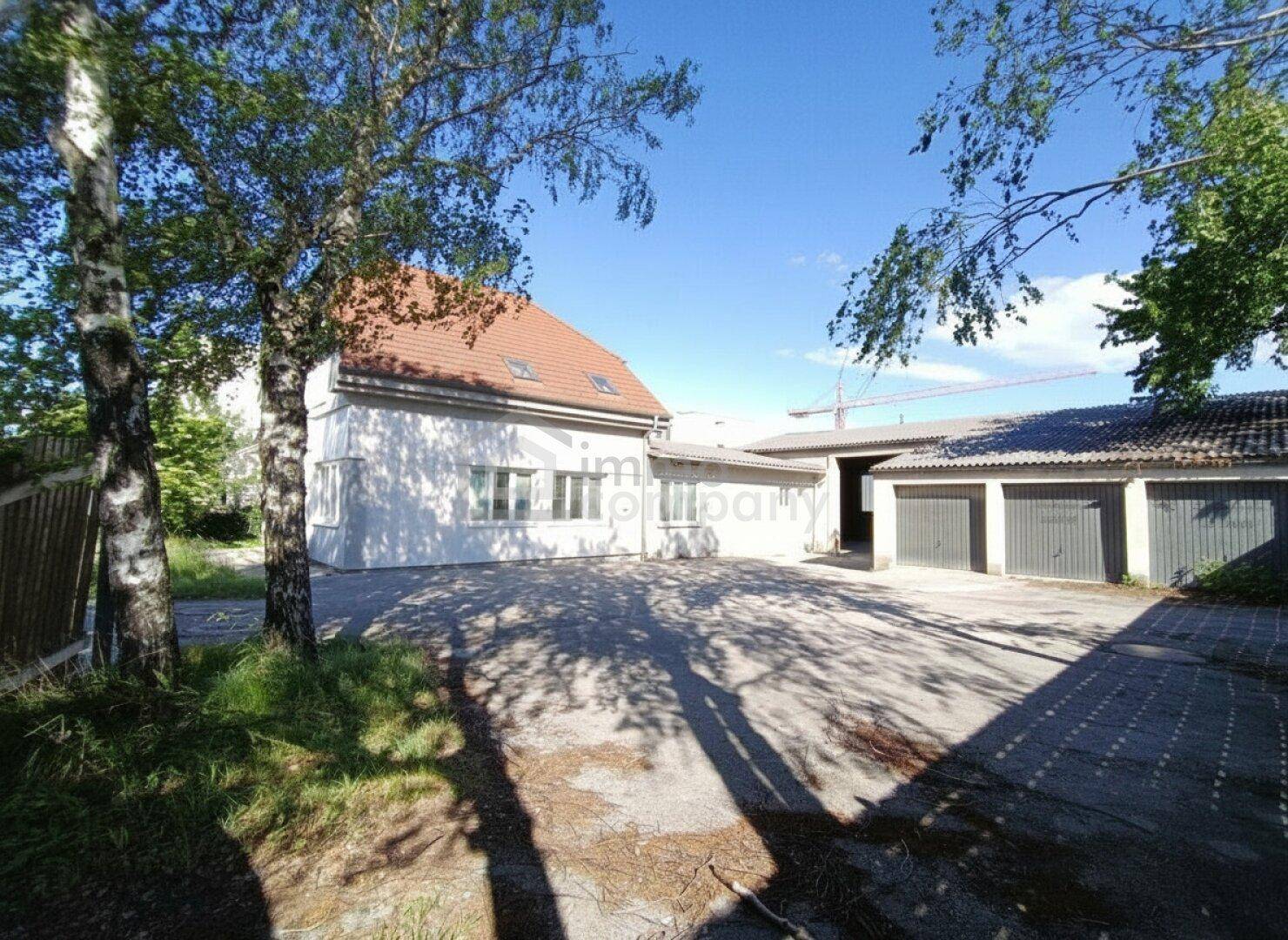 Gebäude mit gepflastertem Hof und mehreren Garagen, umgeben von Bäumen und Grünflächen.