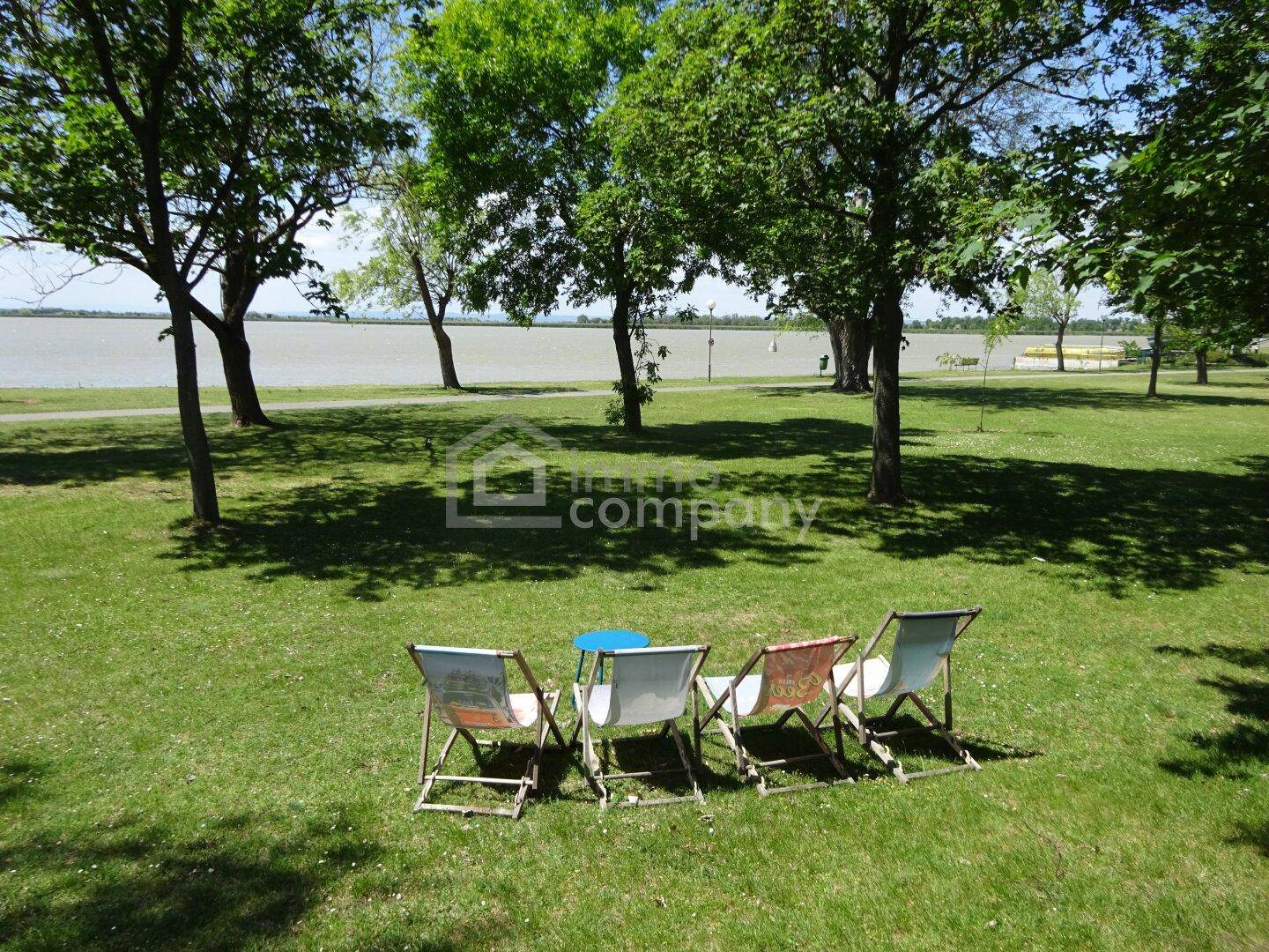 Gepflegter Gartenbereich mit Liegestühlen und Blick auf den See unter schattenspendenden Bäumen.