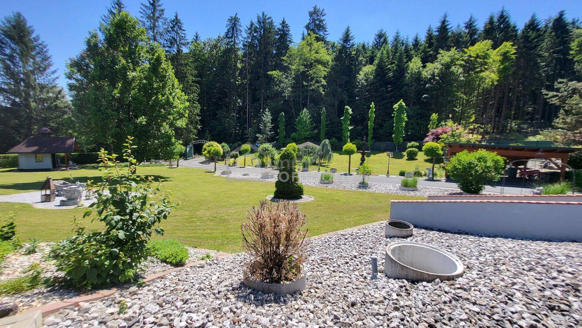 Ein weitläufiger Garten mit Rasenflächen, Zierbäumen und einem Kiesbereich unter blauem Himmel.