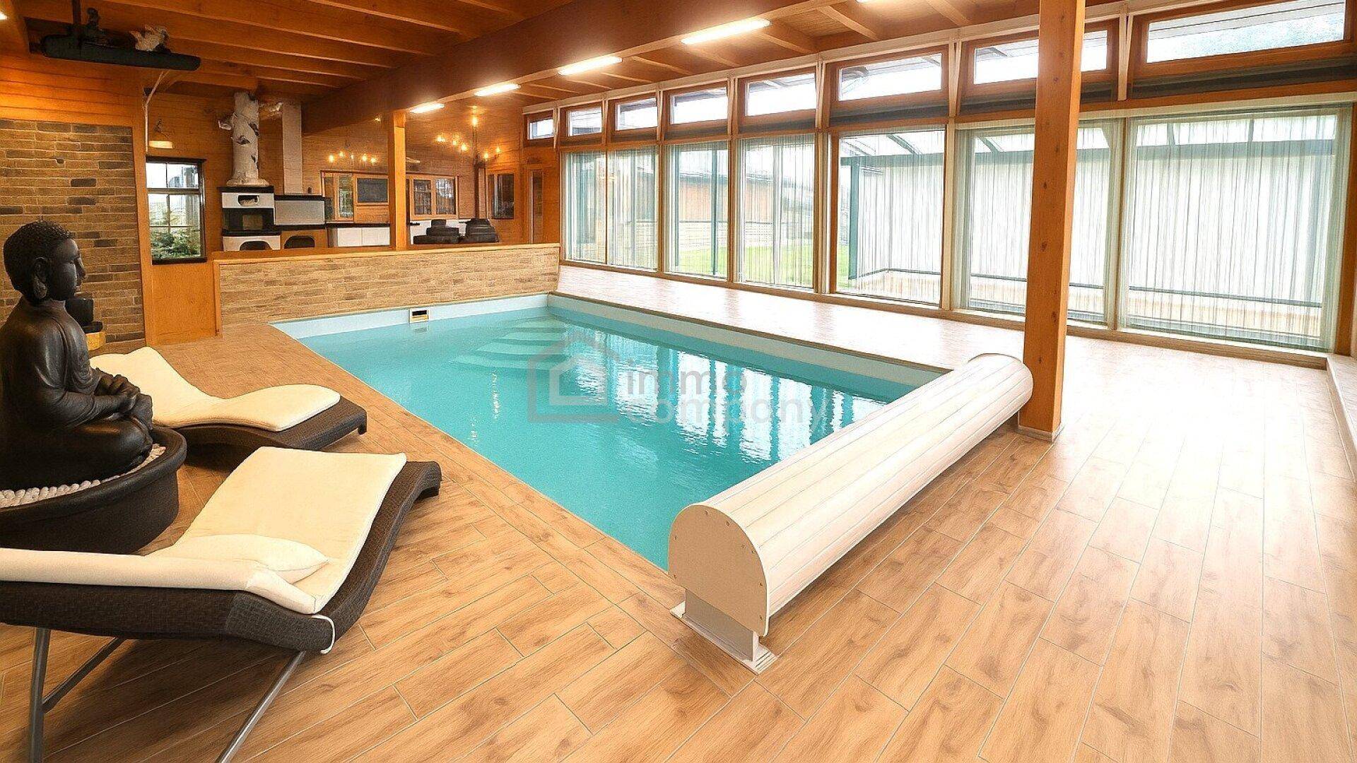 Ein luxuriöser Innenpoolbereich mit Holzdecken, großen Fenstern und bequemen Liegestühlen.